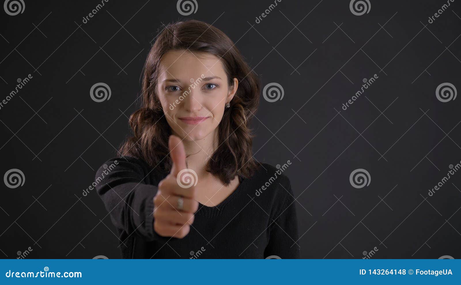 portrait of cute young brunette woman gesturing finger-up sign smilingly to show like and respect on black background.