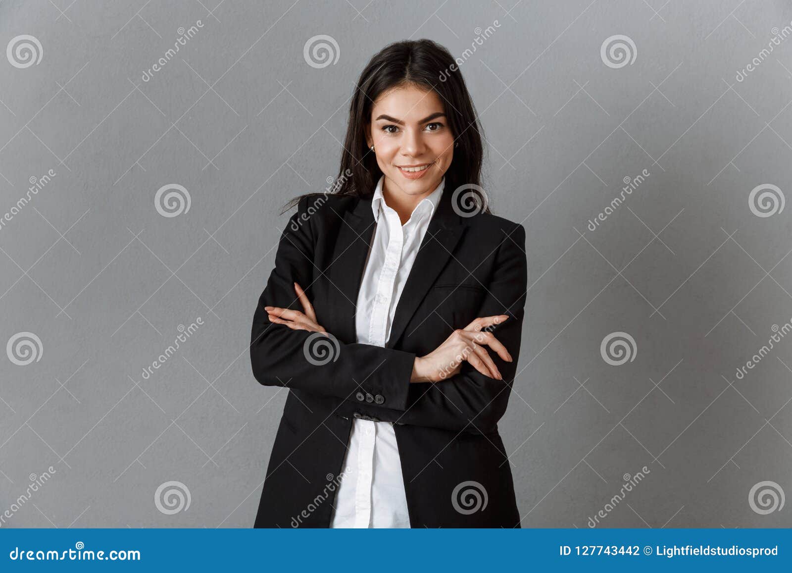 Portrait de femme d'affaires de sourire dans le costume avec des bras croisés contre le contexte gris de mur
