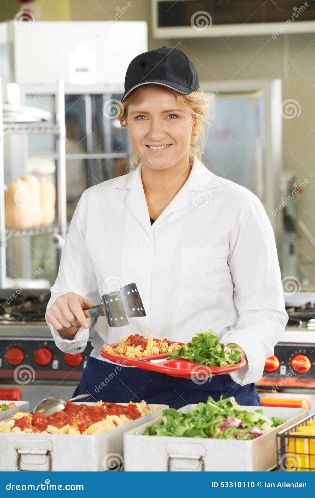 Portrait of Dinner Lady Serving Meal in School Cafeteria Stock Photo