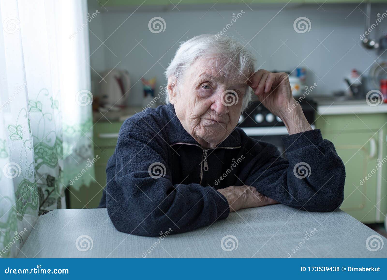 Portrait of an Elderly Woman Sitting at the Table in Kitchen Stock