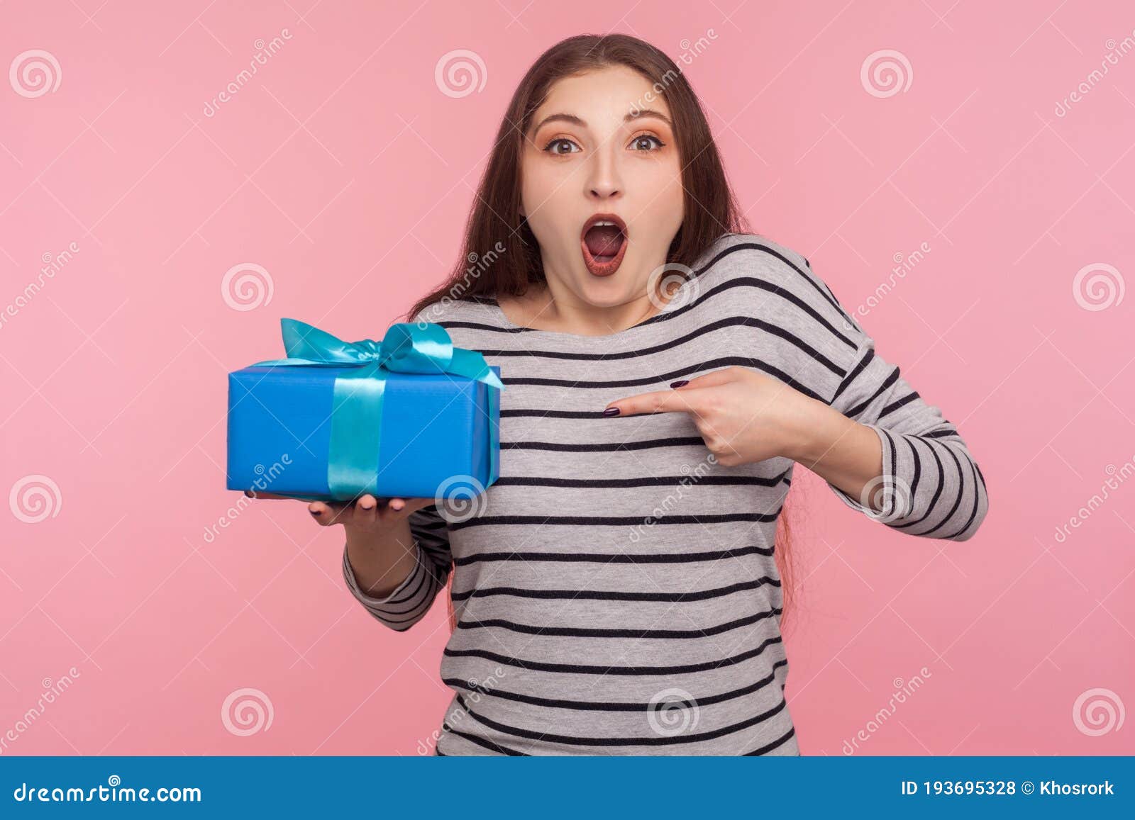 portrait of excited amazed woman in striped sweatshirt pointing at birthday gift and looking surprised