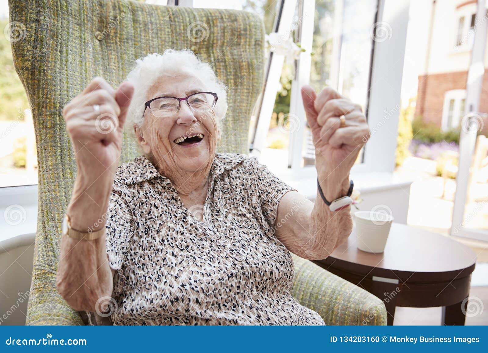 portrait of excited senior woman sitting in chair in lounge of retirement home