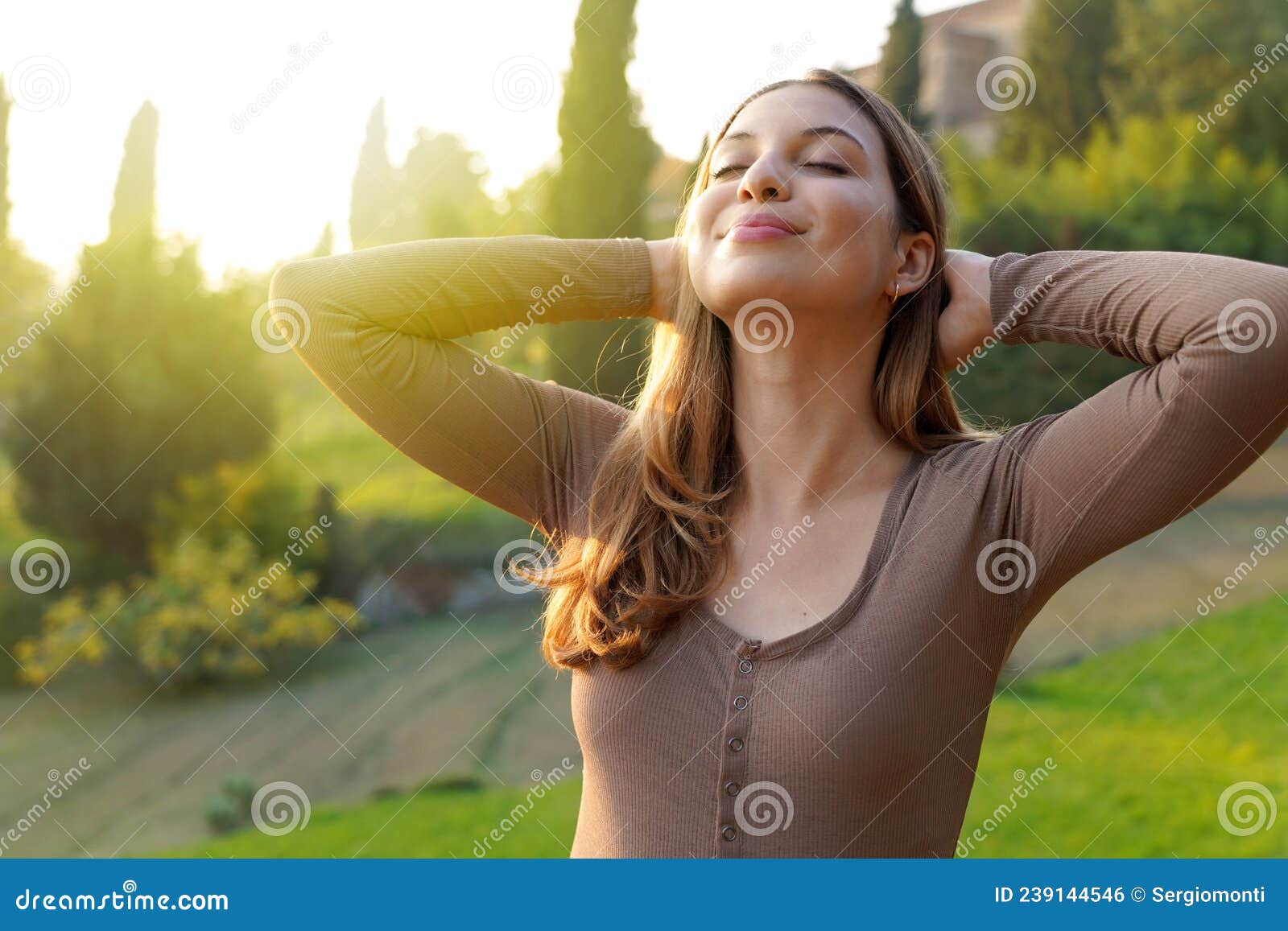 portrait of free woman breathing fresh air in nature. happy girl with hands behind her head in bliss. relaxing, quietness outdoor