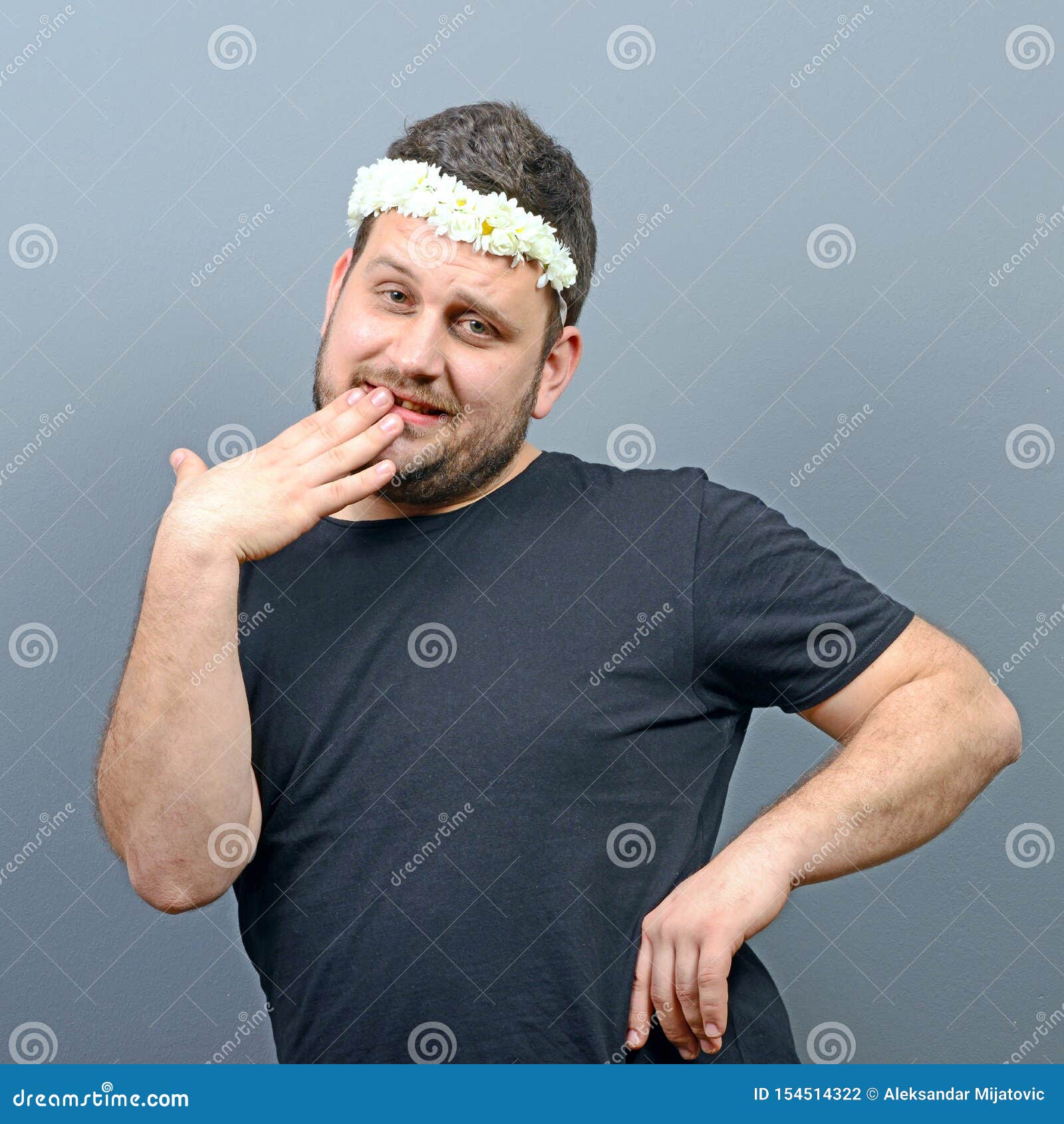 portrait of funny chubby man wearing flower wreath on head and behaving feminine against gray background