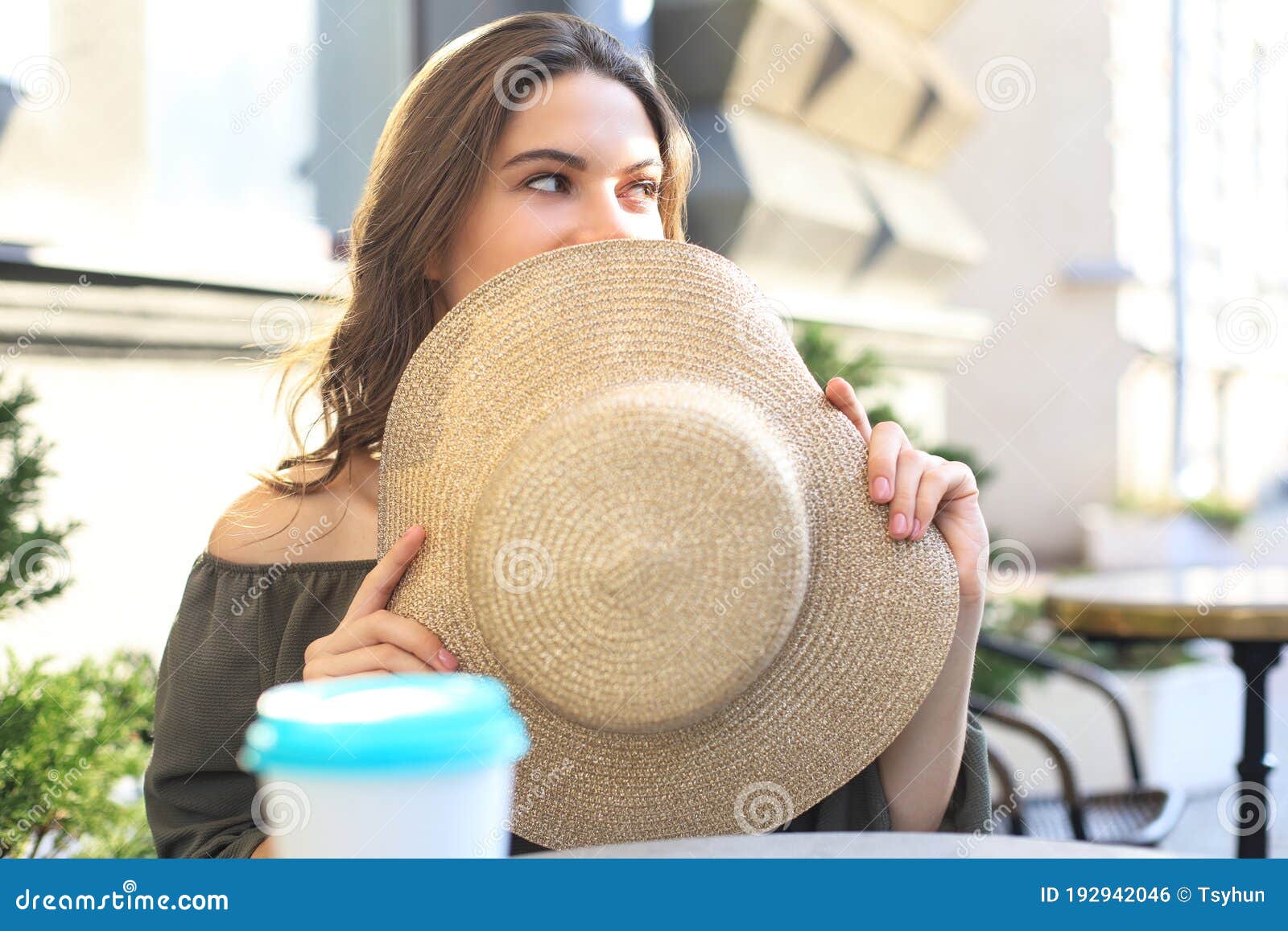 Portrait Of A Girl Hiding Her Face Behind A Straw Hat While Sitting In