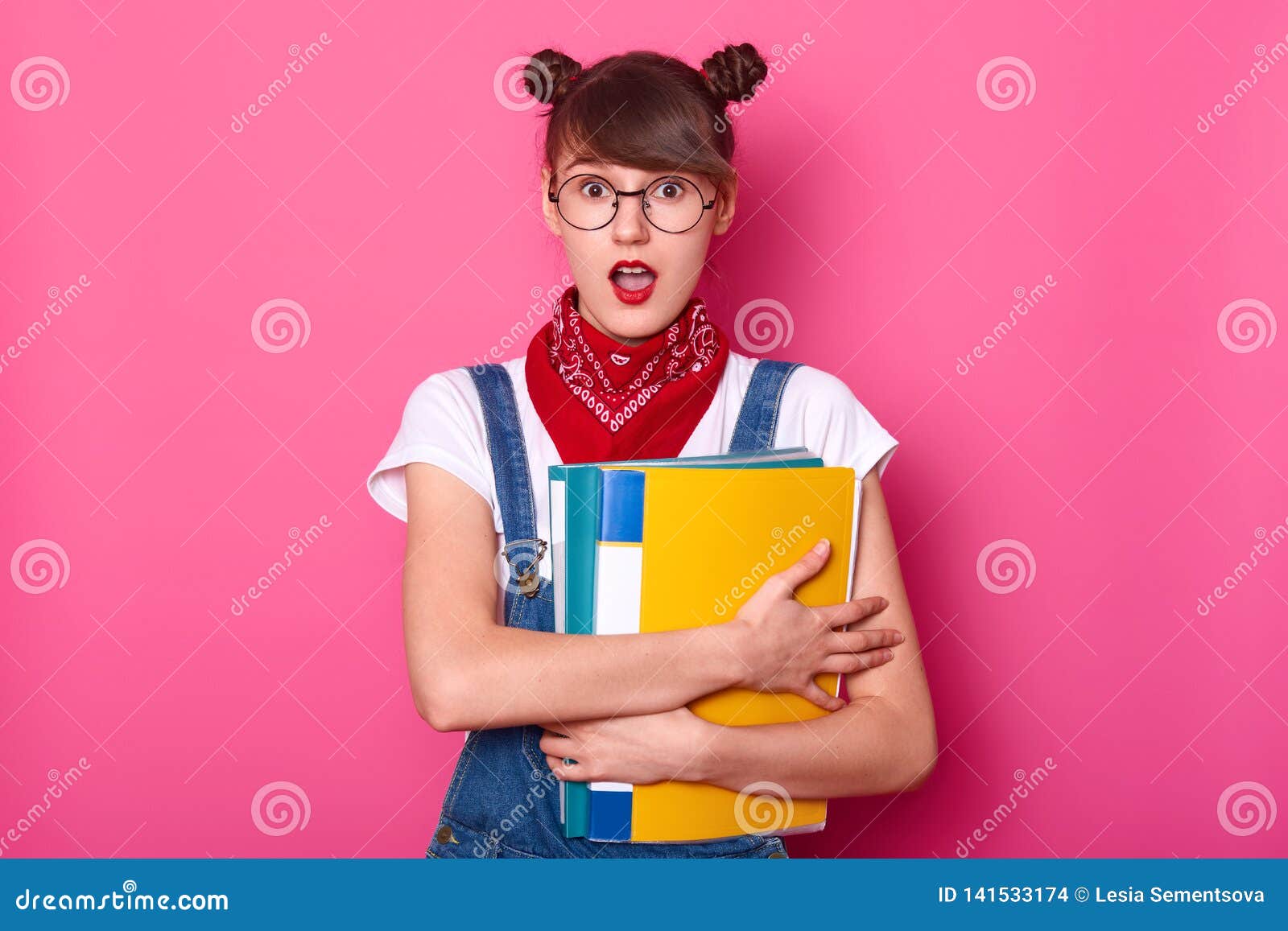 portrait of good looking attractive girl emblaces two colurful folders for papers. teen looks surprised, stands with opened mouth