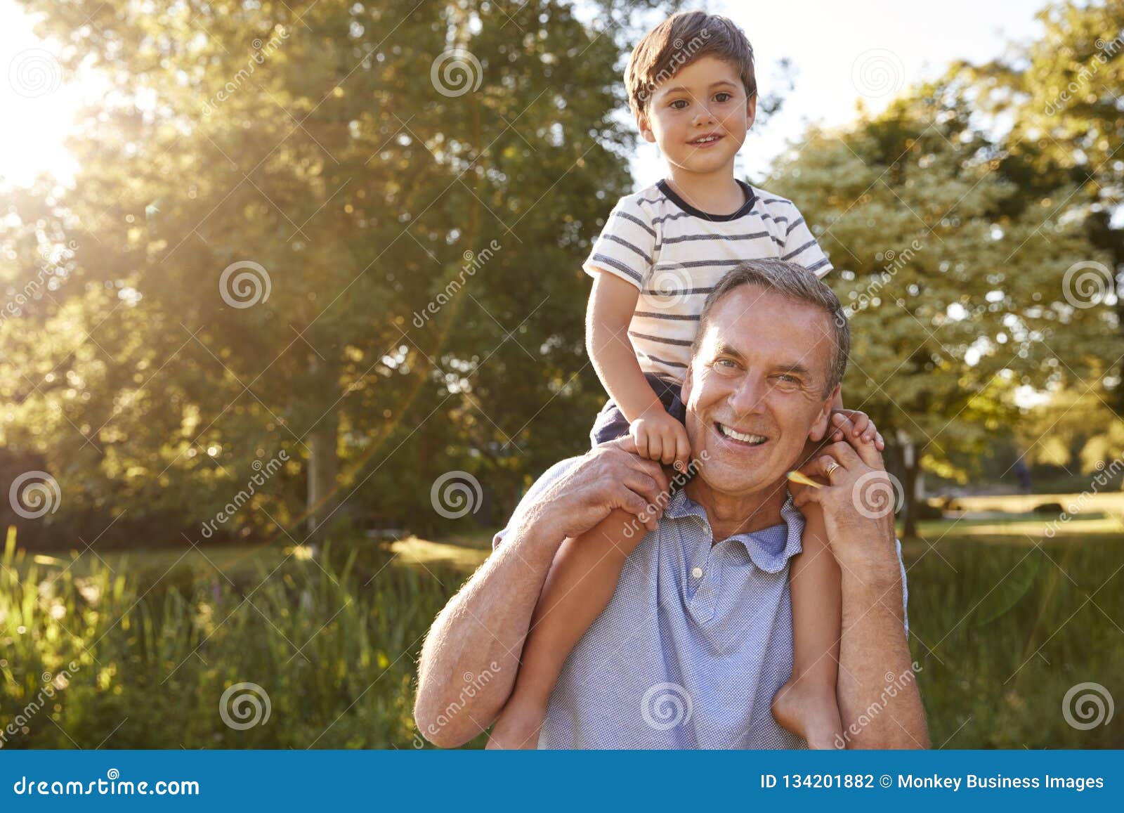 Portrait of Grandfather Giving Grandson Ride on Shoulders in Summer