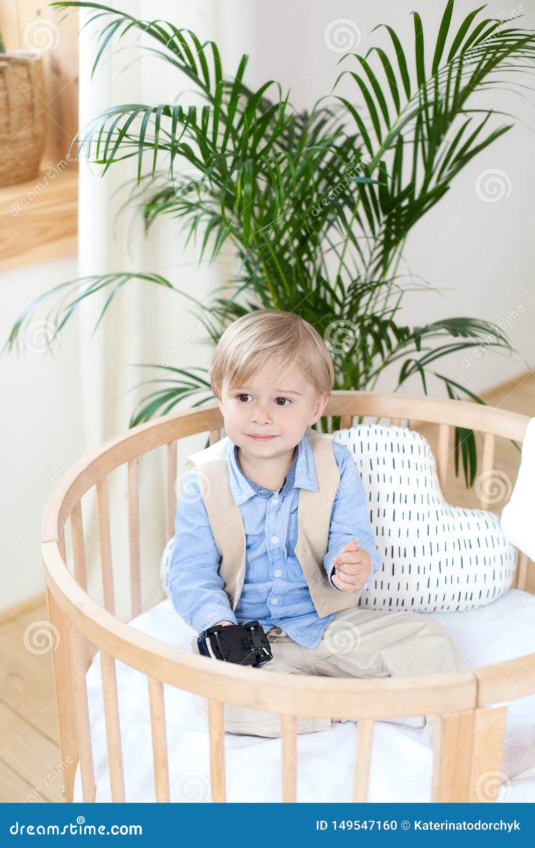 portrait of a happy boy playing in a baby cot. the boy sits alone in a crib in the nursery. lonely baby stay in the crib. waif chi