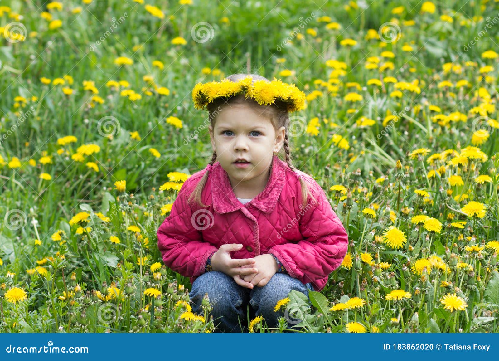 Portrait of happy caucasian child of four years old with wreath on head sitting on meadow of dandelions looking at camera outside
