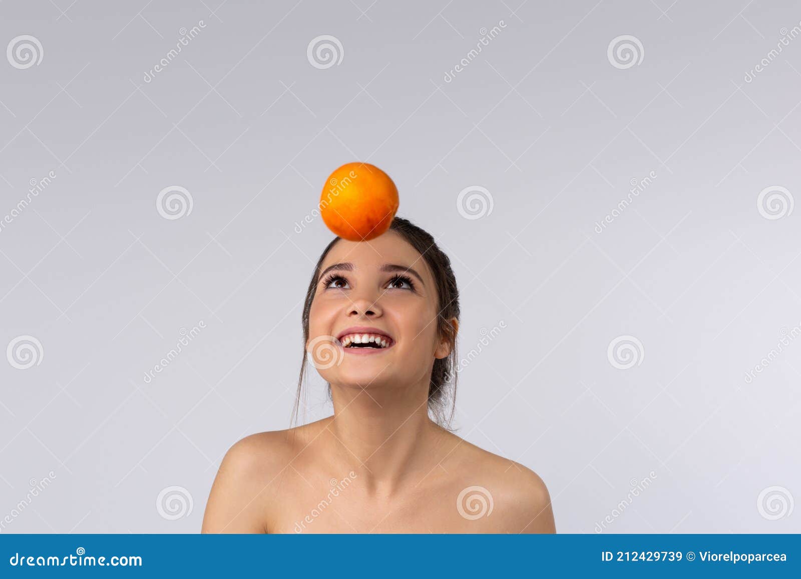 Portrait of a Happy Caucasian Girl Throwing Up an Orange on a Gray