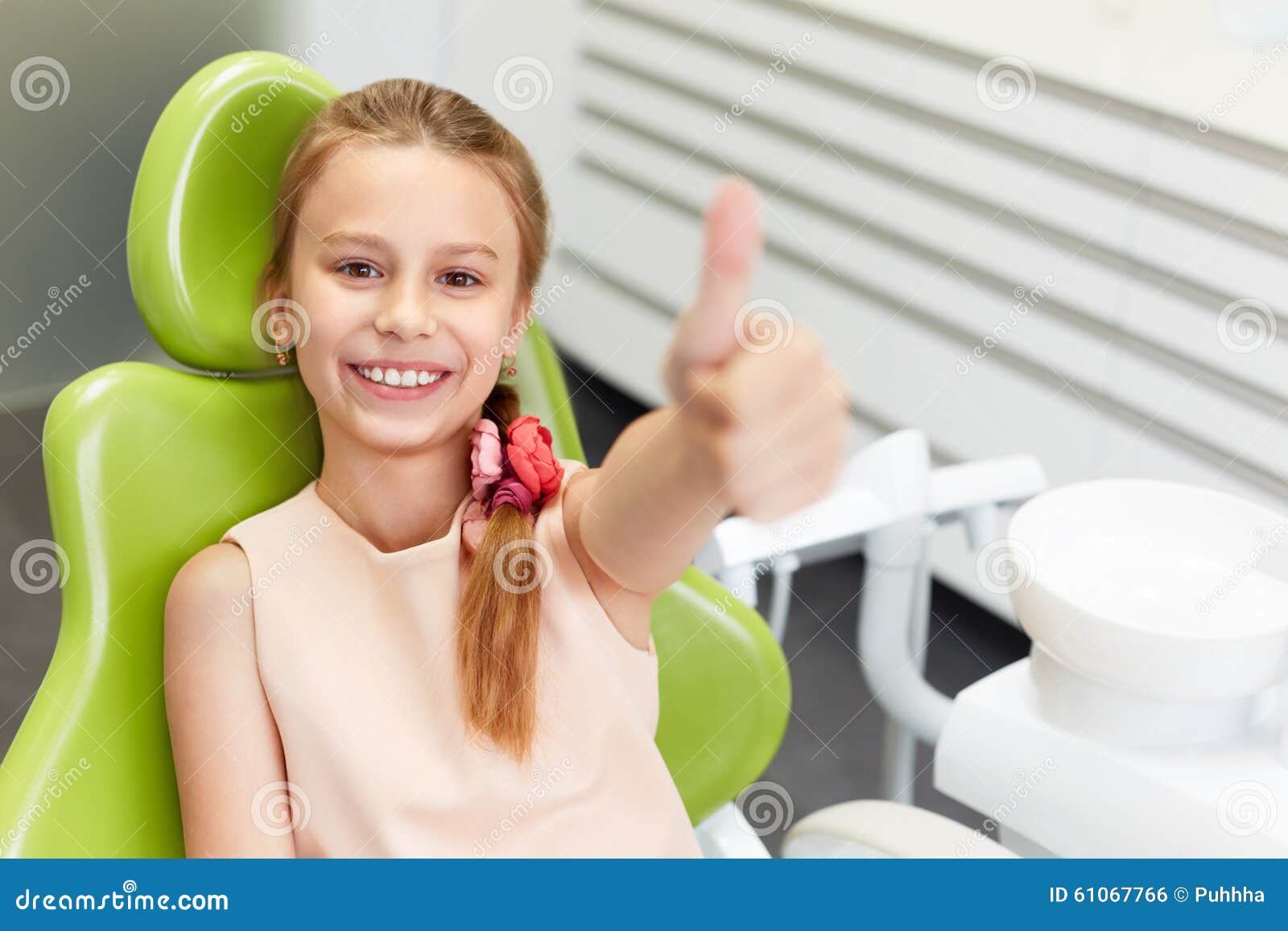 portrait of happy girl shows thumb up gesture at dental clinic