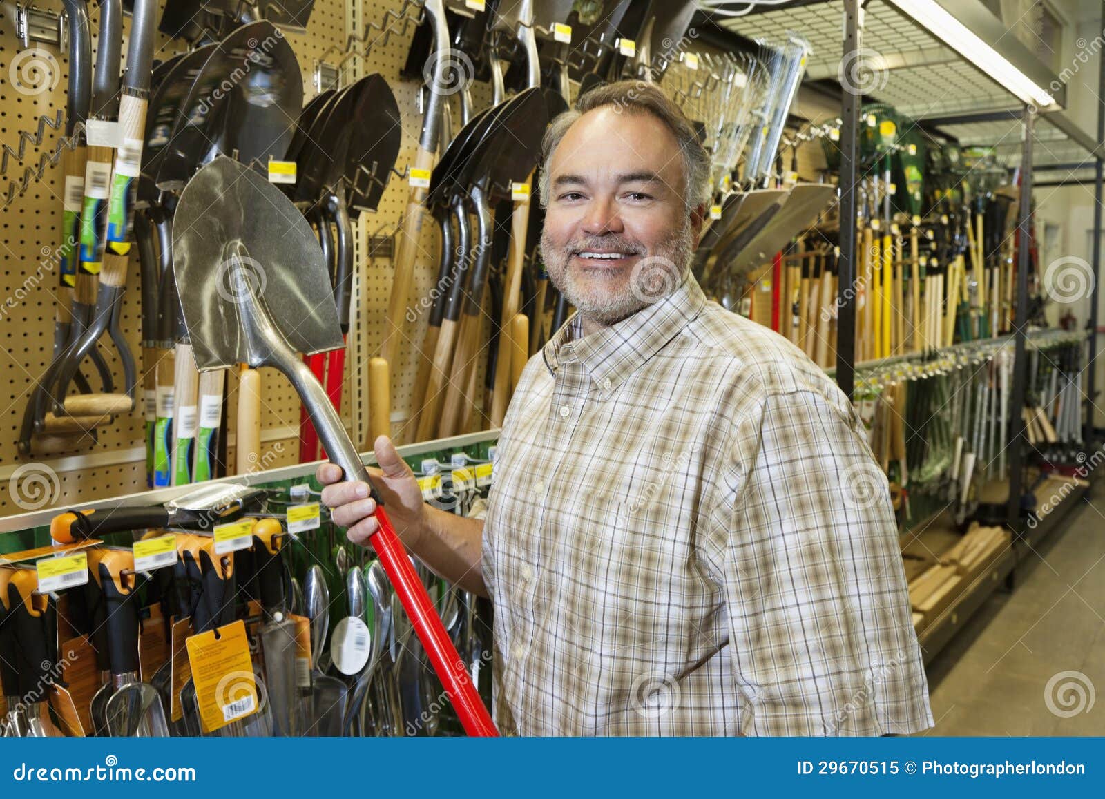 portrait of a happy mature man holding shovel in hardware store