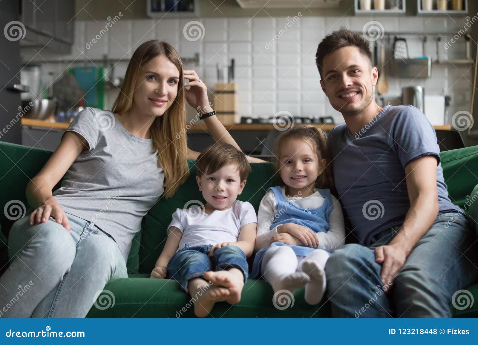 Portrait Of Happy Parents With Cute Kids Sitting On Sofa Stock Photo