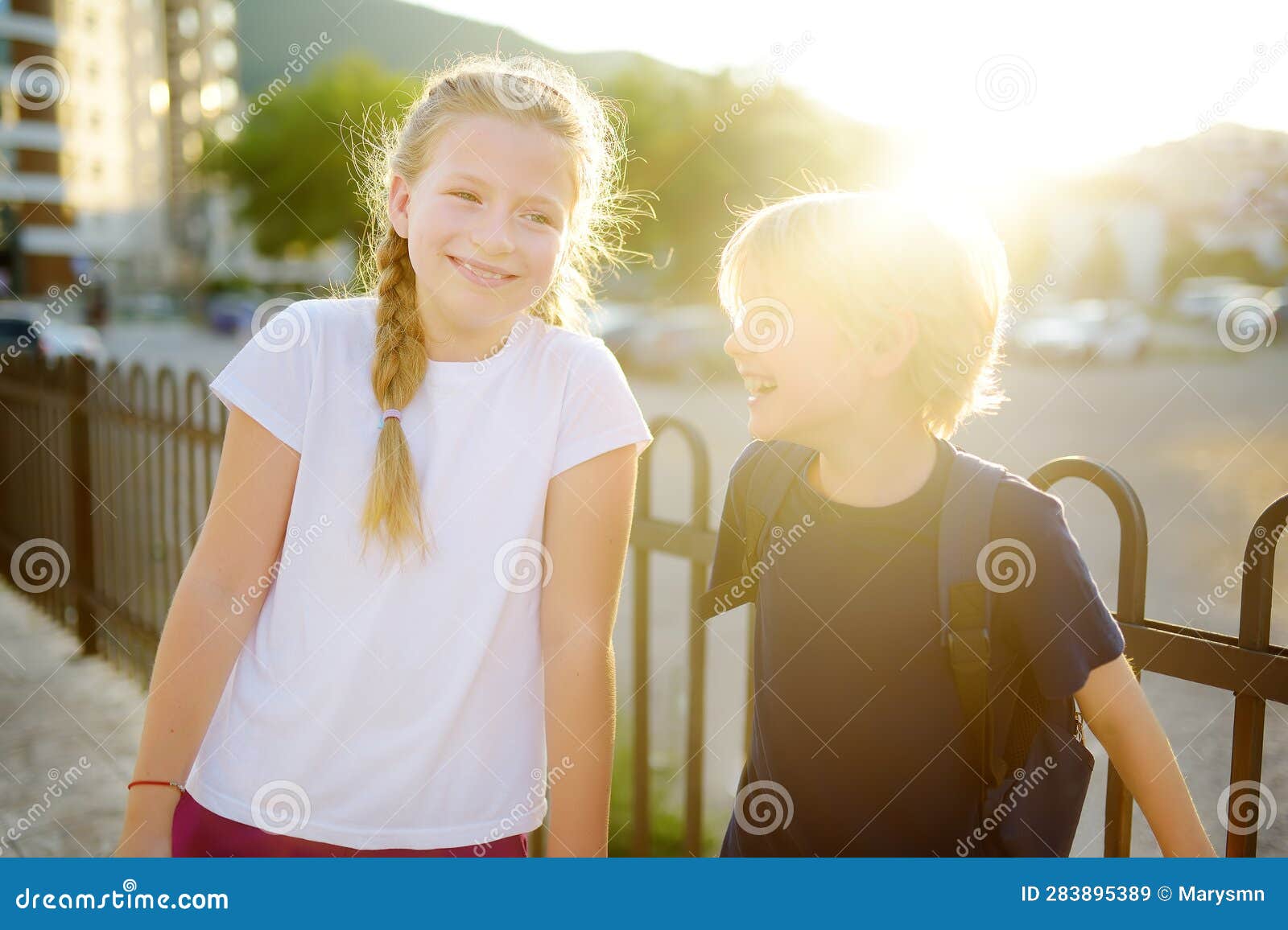portrait of a happy preteens girl and boy on a city street during a summer sunset. friends are walking together. first love