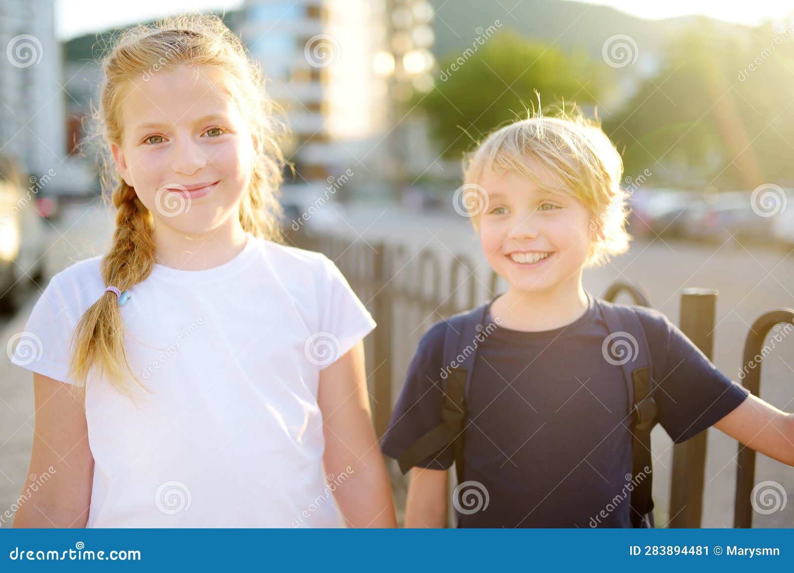 portrait of a happy preteens girl and boy on a city street during a summer sunset. friends are walking together