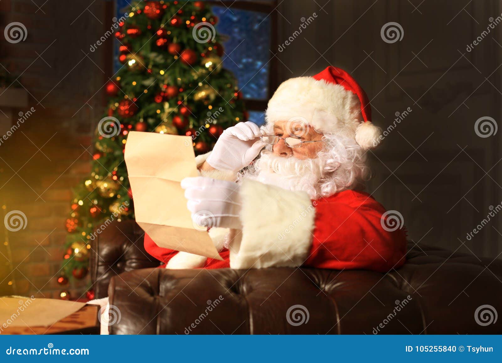 portrait of happy santa claus sitting at his room at home near christmas tree and reading christmas letter or wish list.