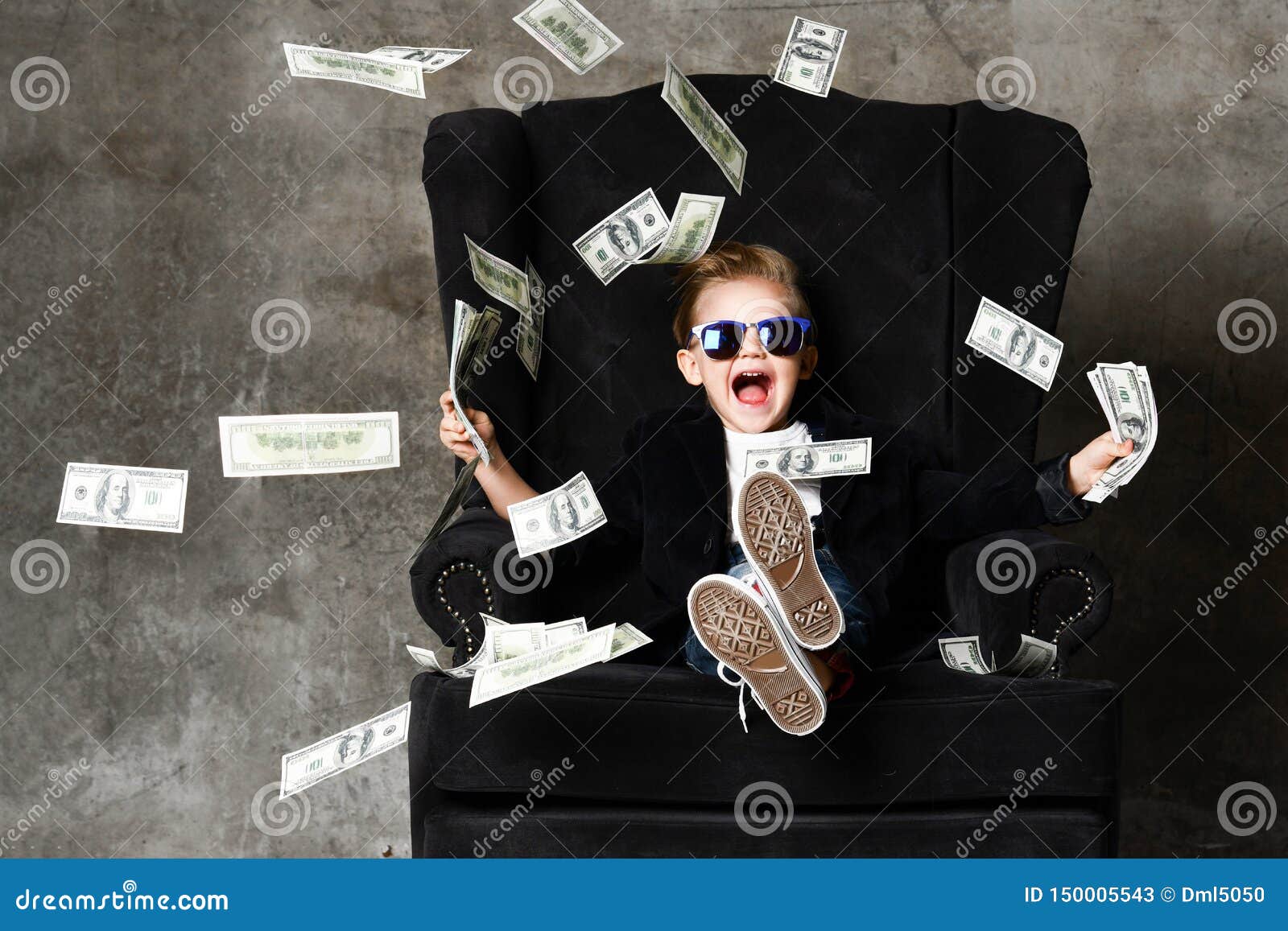 portrait of happy shouting self-confident rich kid boy millionaire sitting in luxury armchair and throwing money dollars cash