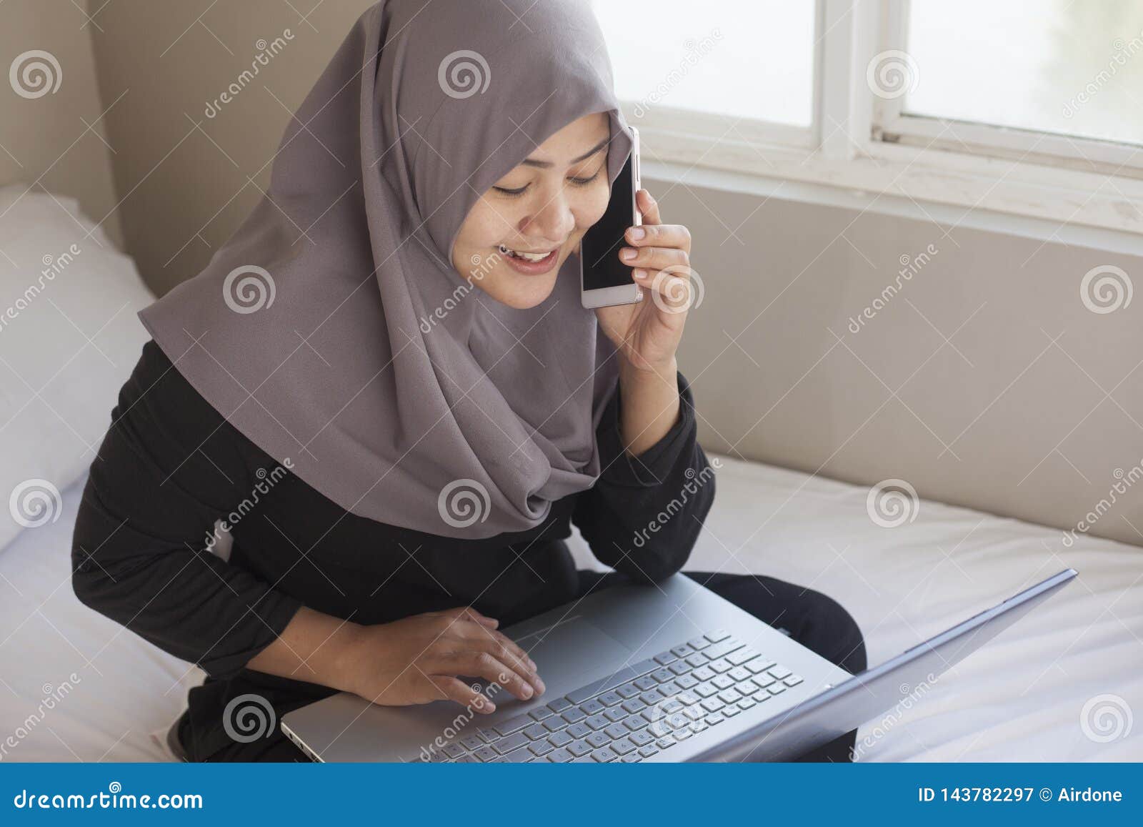 Happy Muslim Woman Working with Laptop and Smart Phone in Her Bedroom ...
