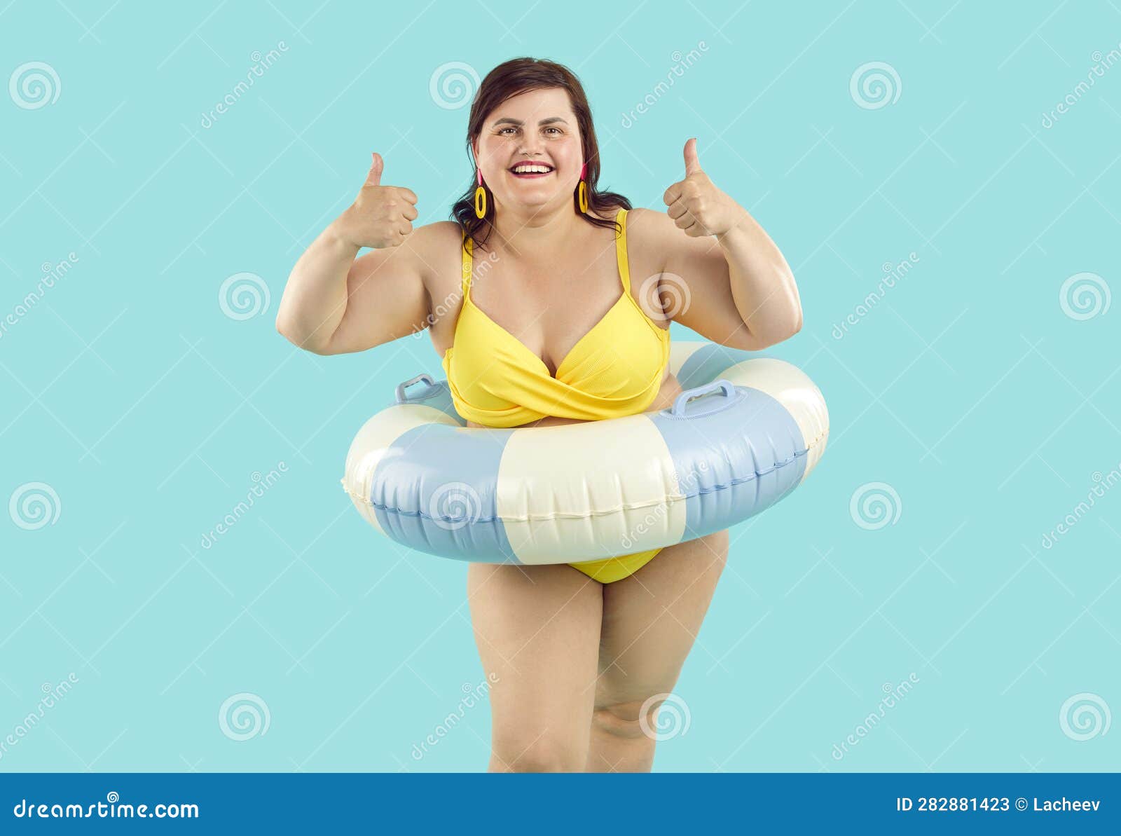 portrait happy smiling fat woman beach rubber ring wearing yellow swimsuit showing thumb up sign isolated blue studio 282881423