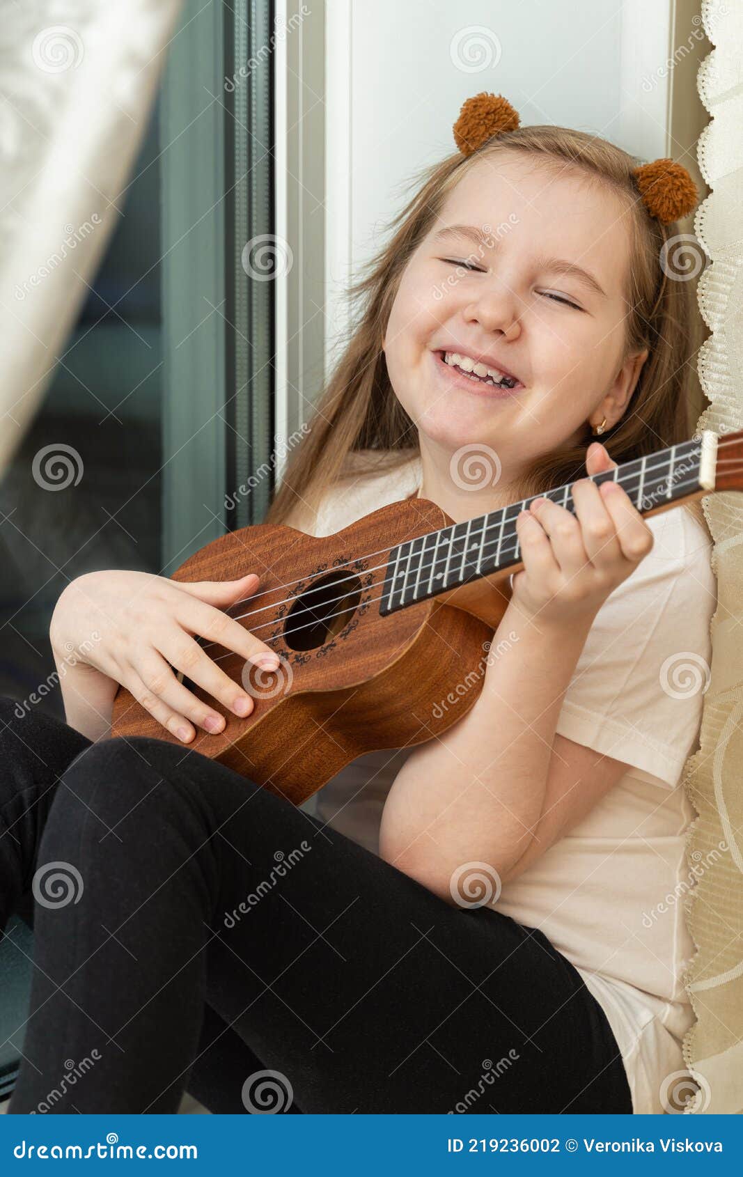 Portrait of Happy Smiling Little Girl in White T-shirt and Black Leggings  Sitting Inside of Home and Playing Ukulele. Stock Photo - Image of  lifestyle, face: 219236002
