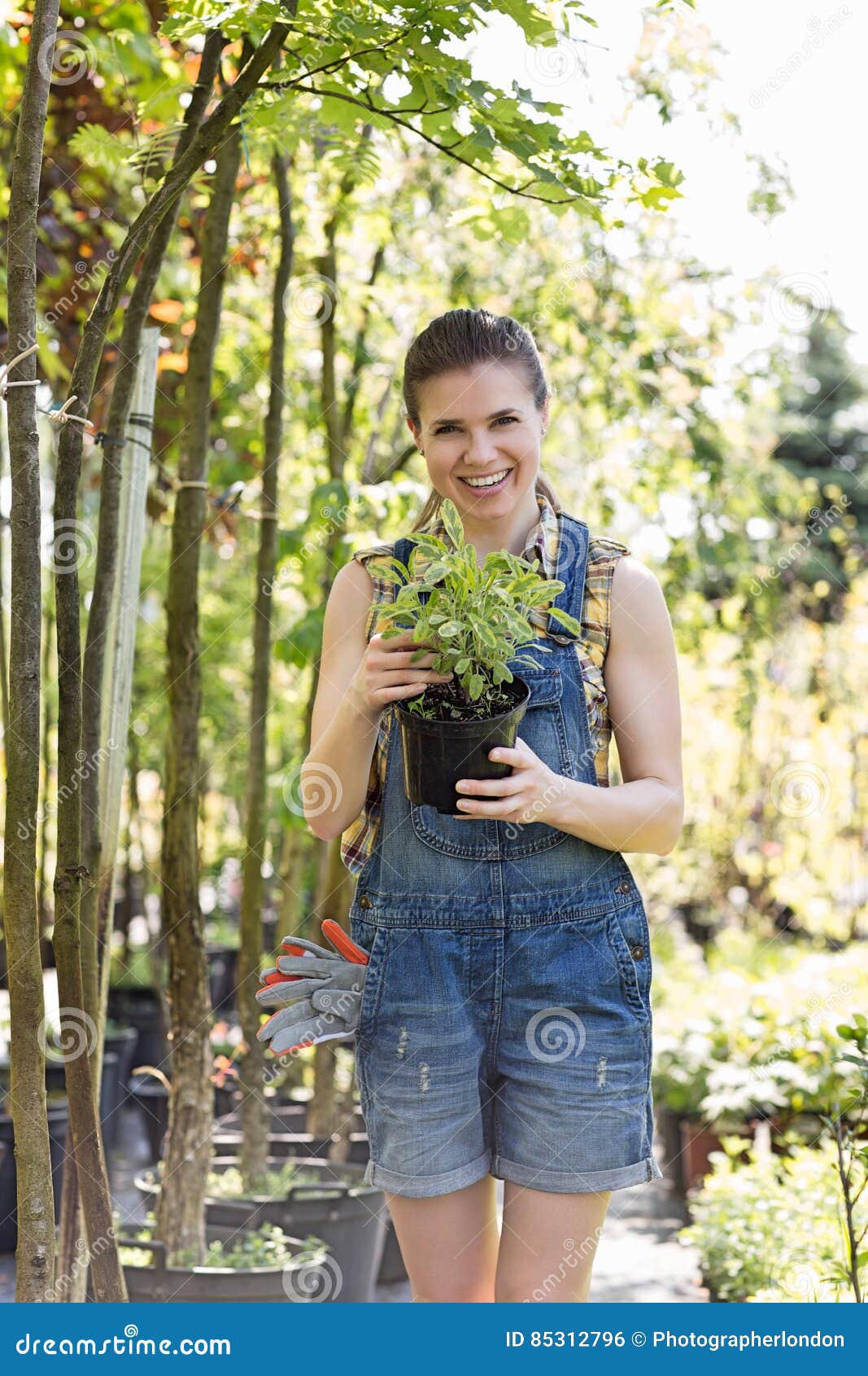 Portrait Of Happy Woman Holding Potted Plant At Garden ...