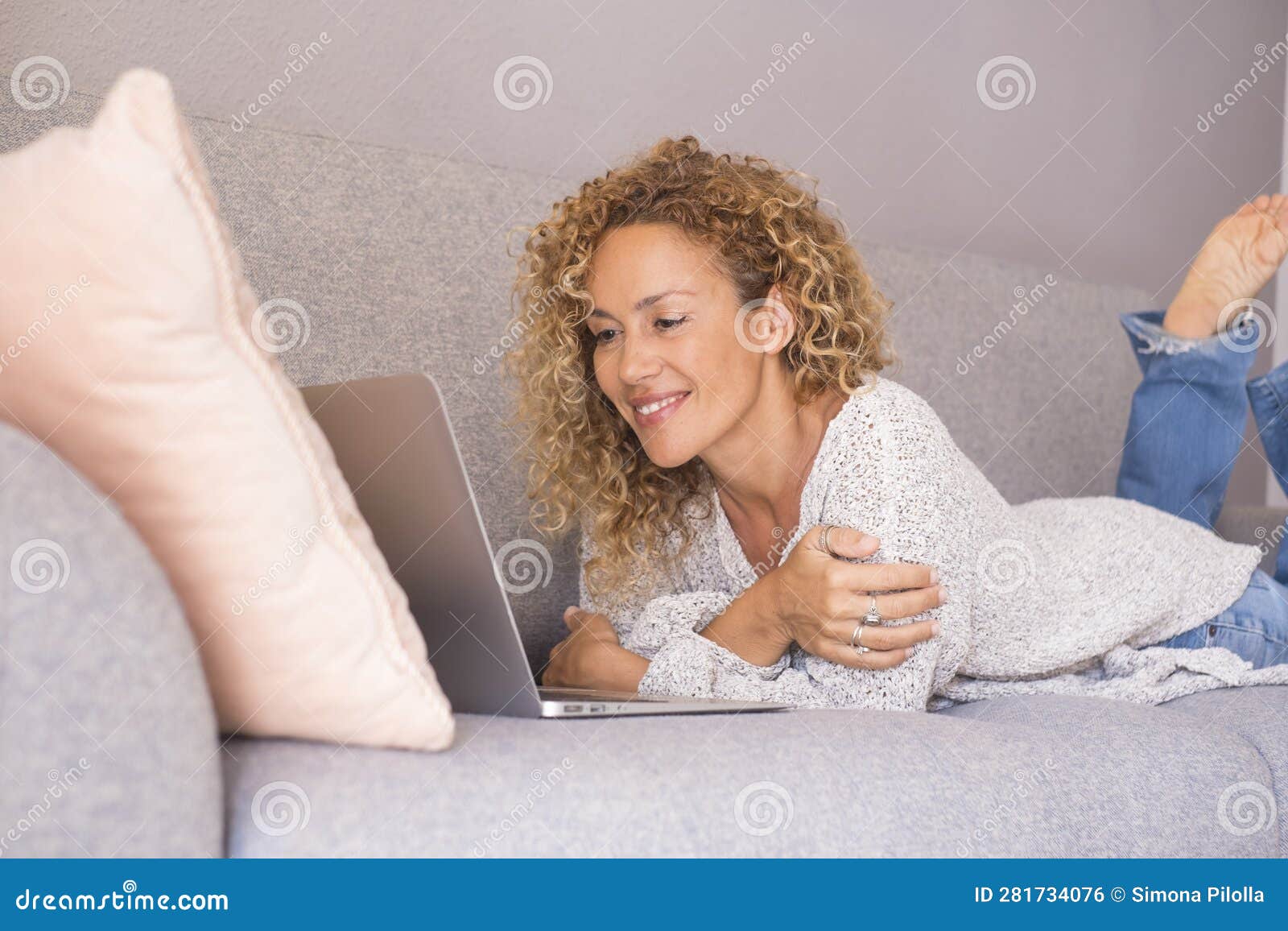 portrait of happy young adult womn using computer laying down on the couch at home in indoor relaxation leisure acitivy alone.