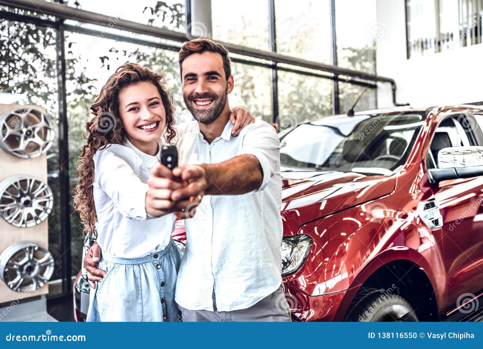 portrait of a happy young couple hugging in a car salon showing car keys to a newly bought vehicle
