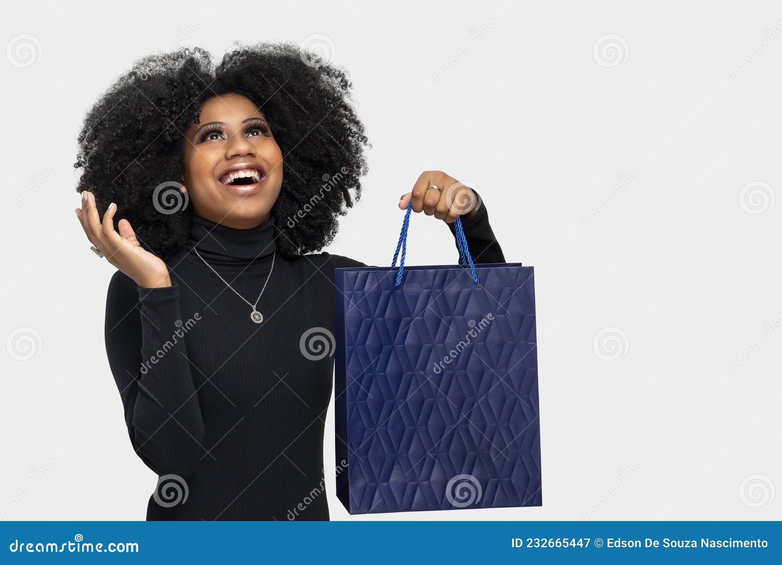 portrait of a happy young woman with big smile looking up holding shopping bag  on gray background, end of year sale or mi