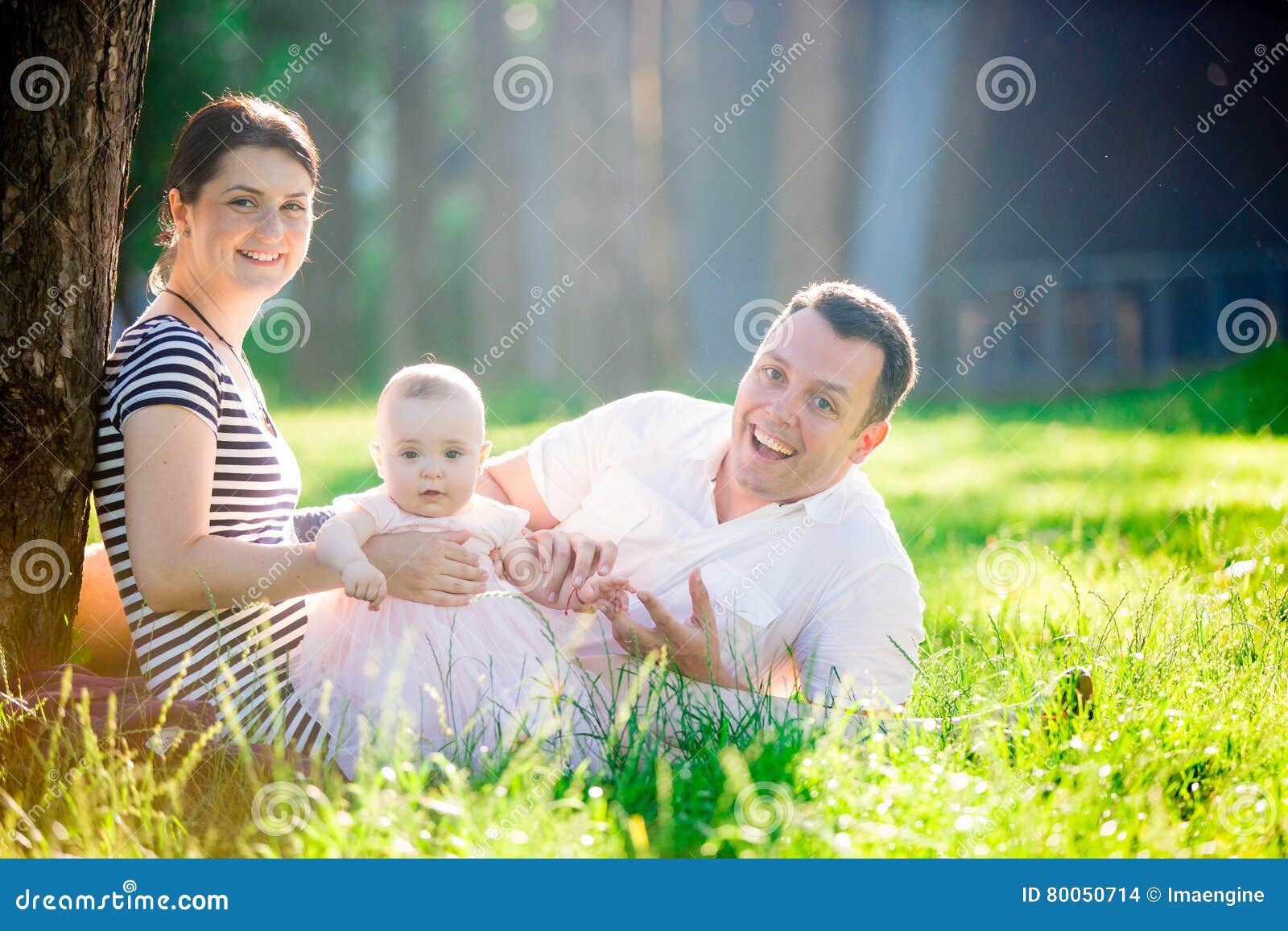 Portrait heureux de Familly. Beau petit bébé s'asseyant sur l'herbe verte d'un pré ensoleillé avec sa maman et papa