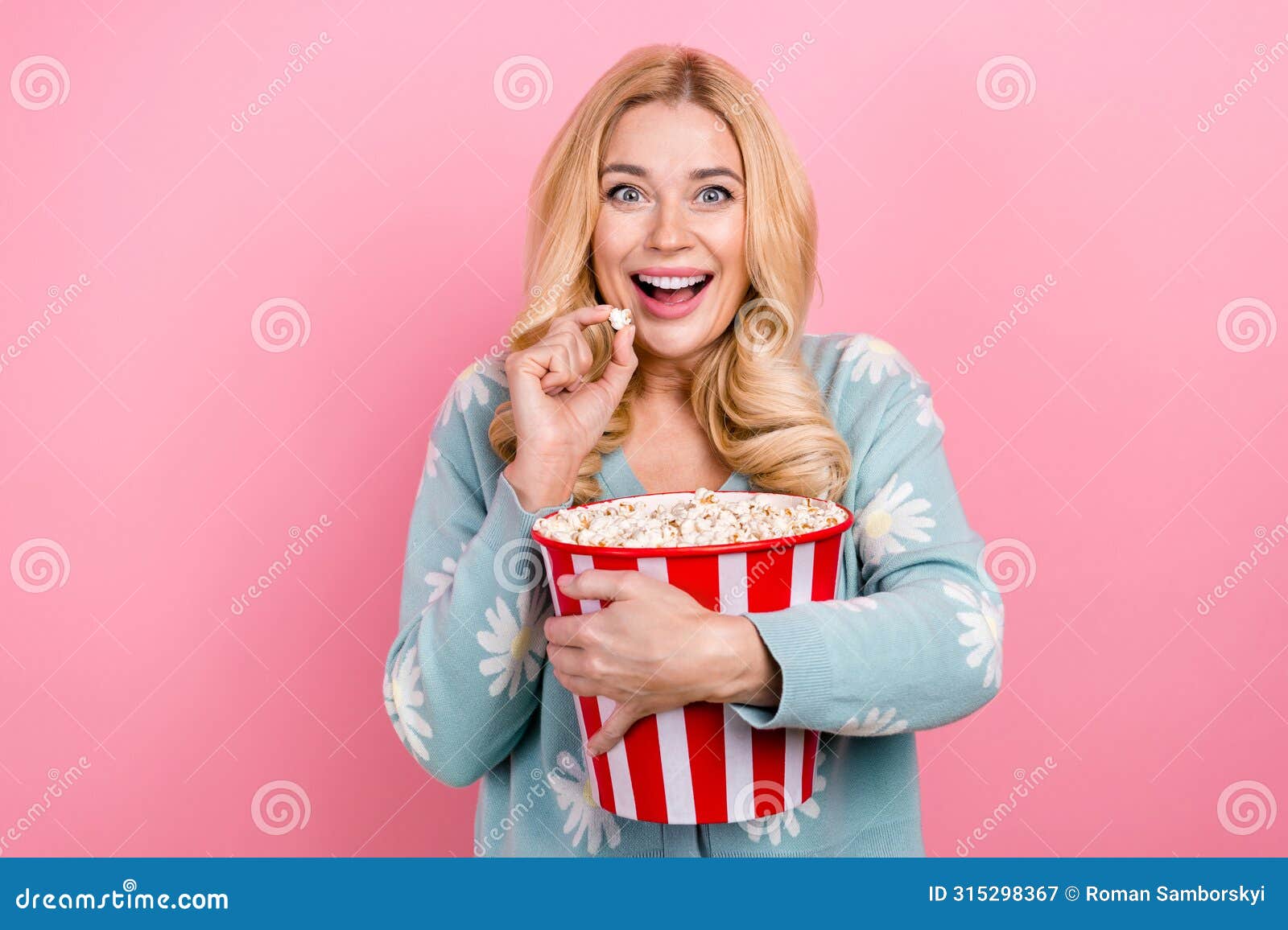 portrait of impressed person with curly hair wear blue cardigan eat popcorn watch intersting movie  on pink