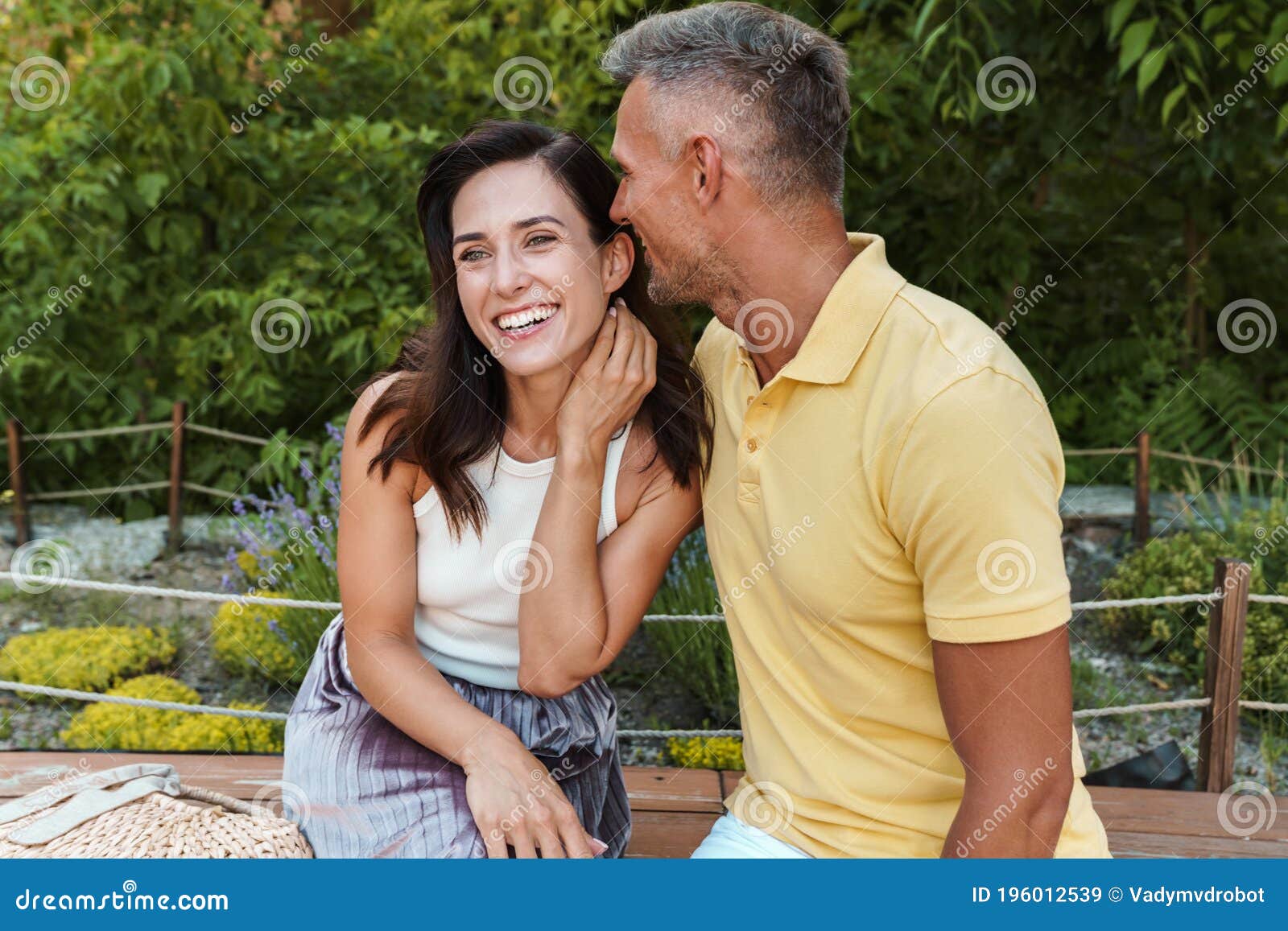 Portrait Of Laughing Middle Aged Couple Hugging While Sitting On Bench In Summer Park Stock