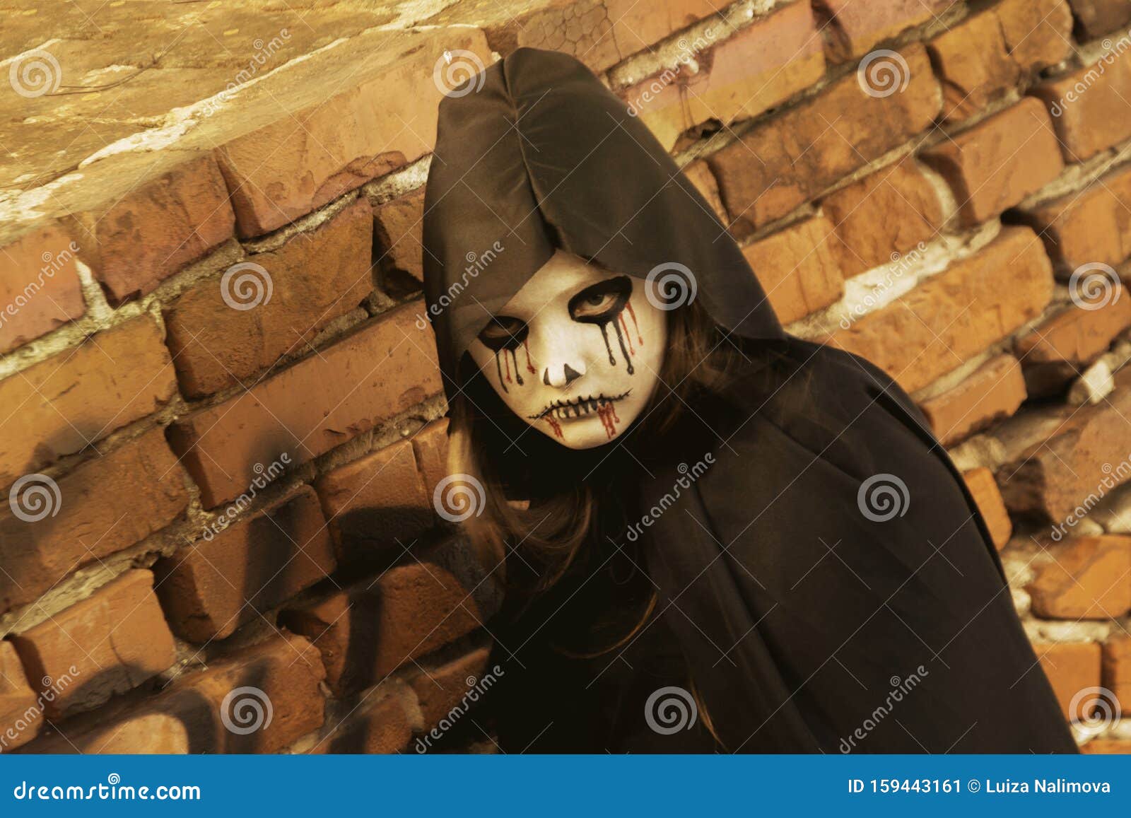 portrait of a little teenager girl in a zombie costum against a brick wall. halloween and day of the dead concept. zombie looks at