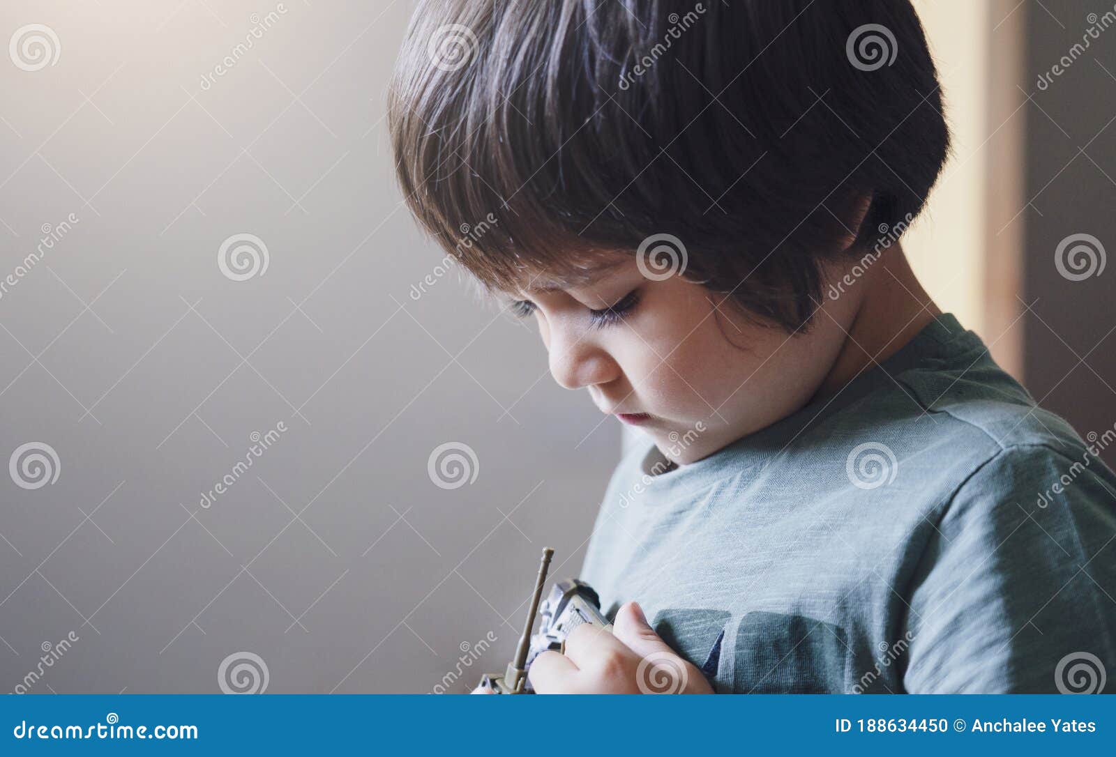 portrait of lonly kid boy with sad face playing alone, bored child looking at tank toy with thinking face