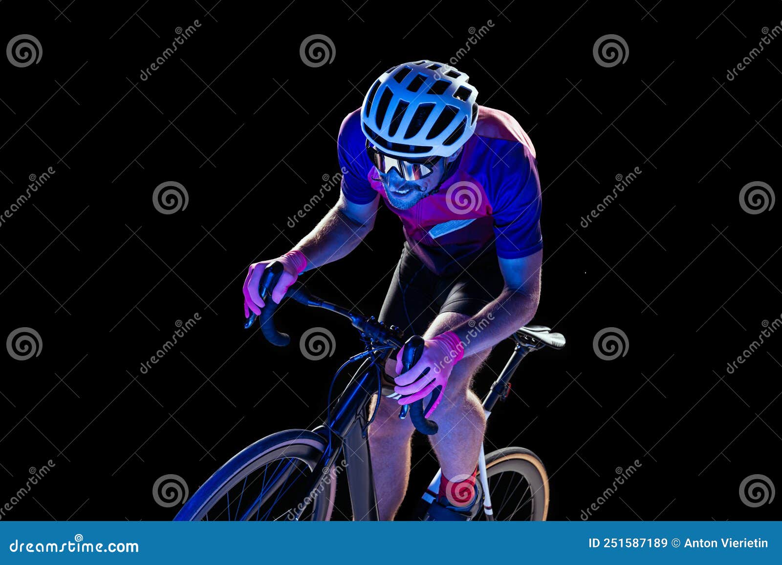 portrait of man, professional cyclist training, riding  over black studio background in neon light. outrunning