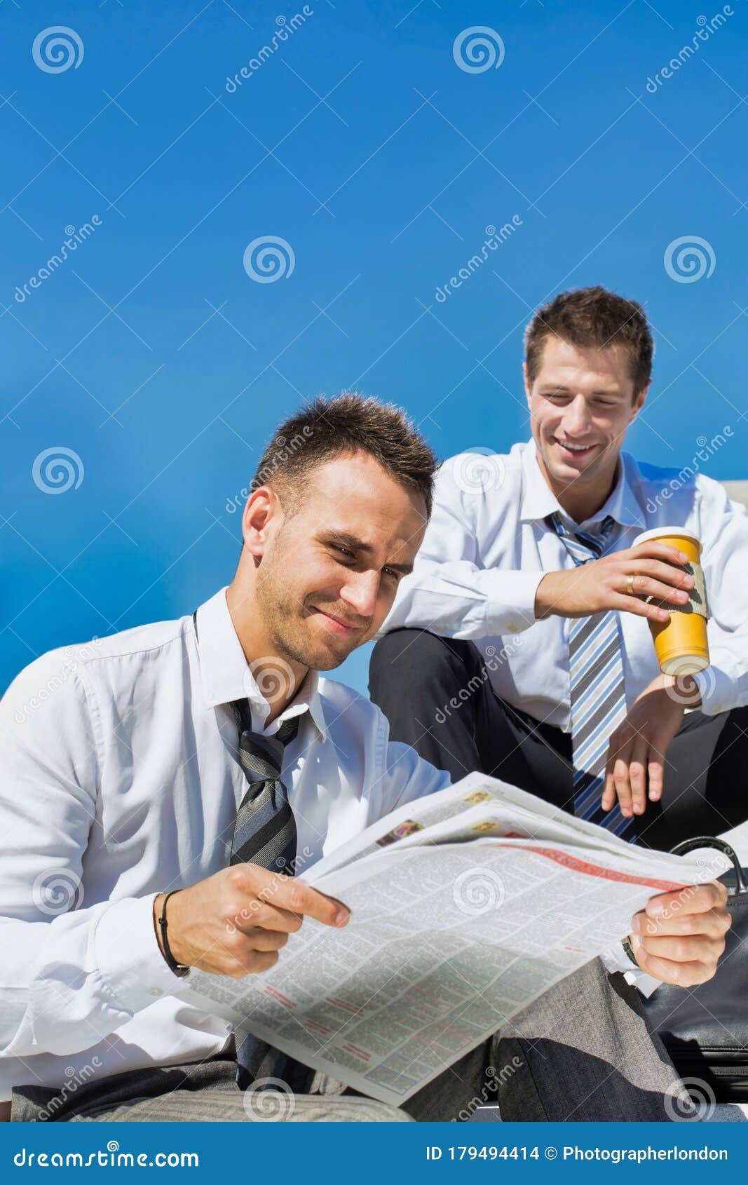 portrait of mature handsome businessman reading newspaper against collegue during break