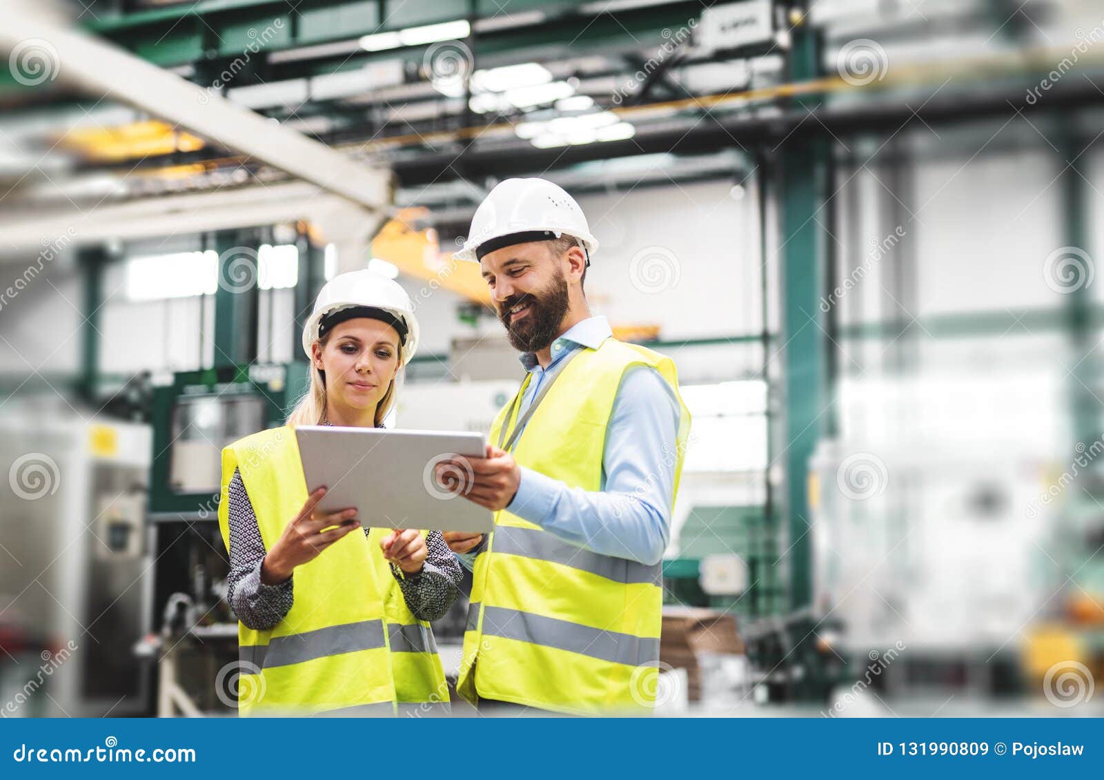 a portrait of an industrial man and woman engineer with tablet in a factory, talking.