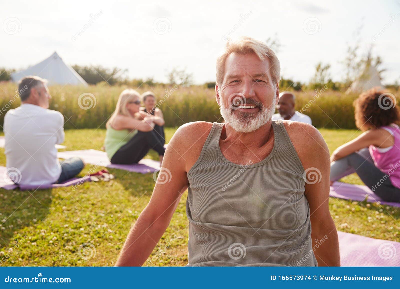 portrait of mature man on outdoor yoga retreat with friends and campsite in background