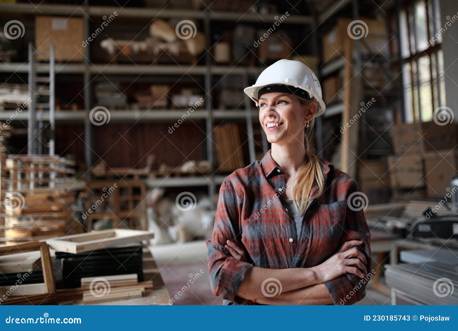 portrait of mid-adult female carpenter standing in carpentery workshop, looking aside and smiling. small business