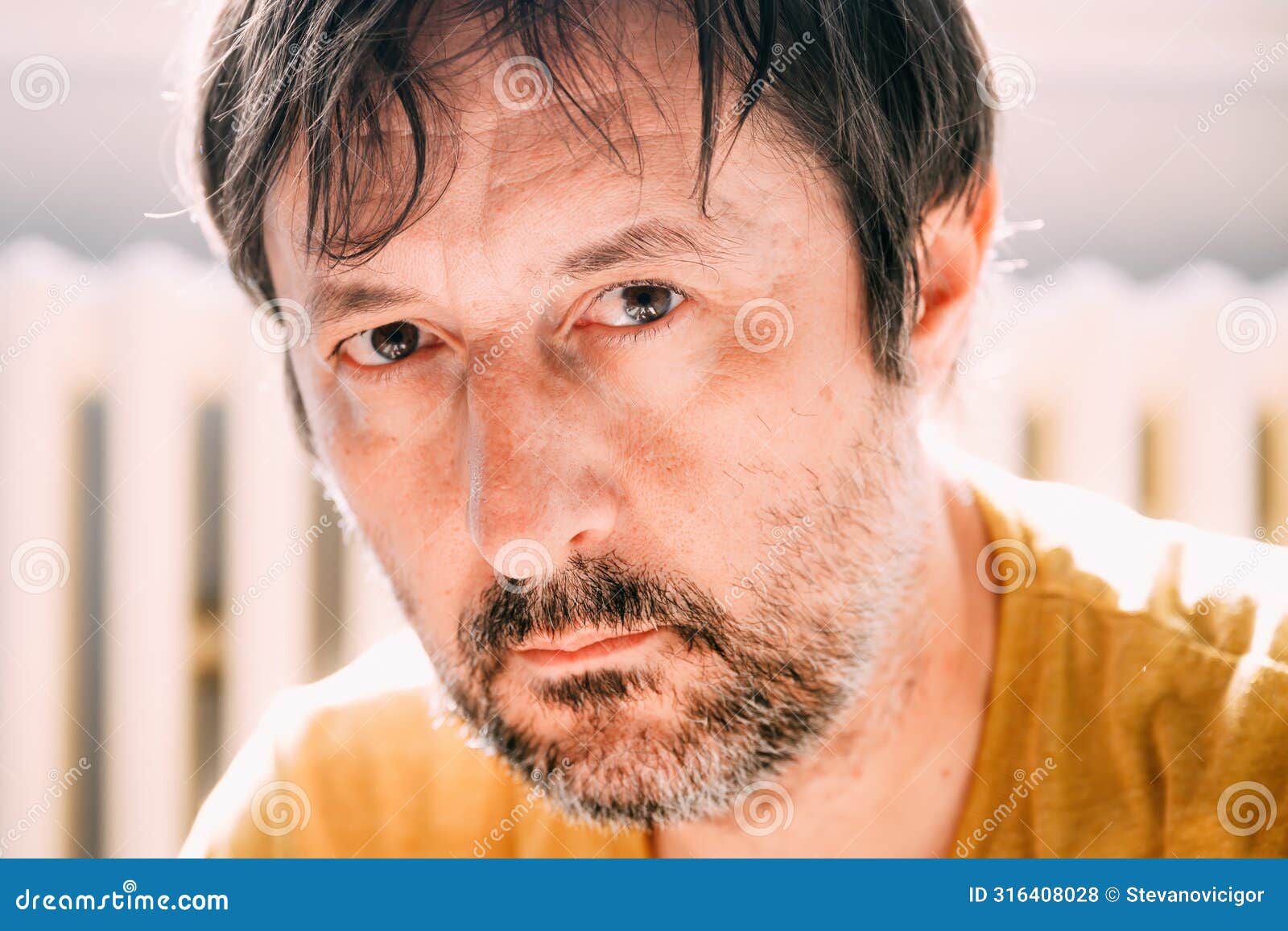 portrait of mid adult unkempt male with beard in late 40s looking at camera in his living room