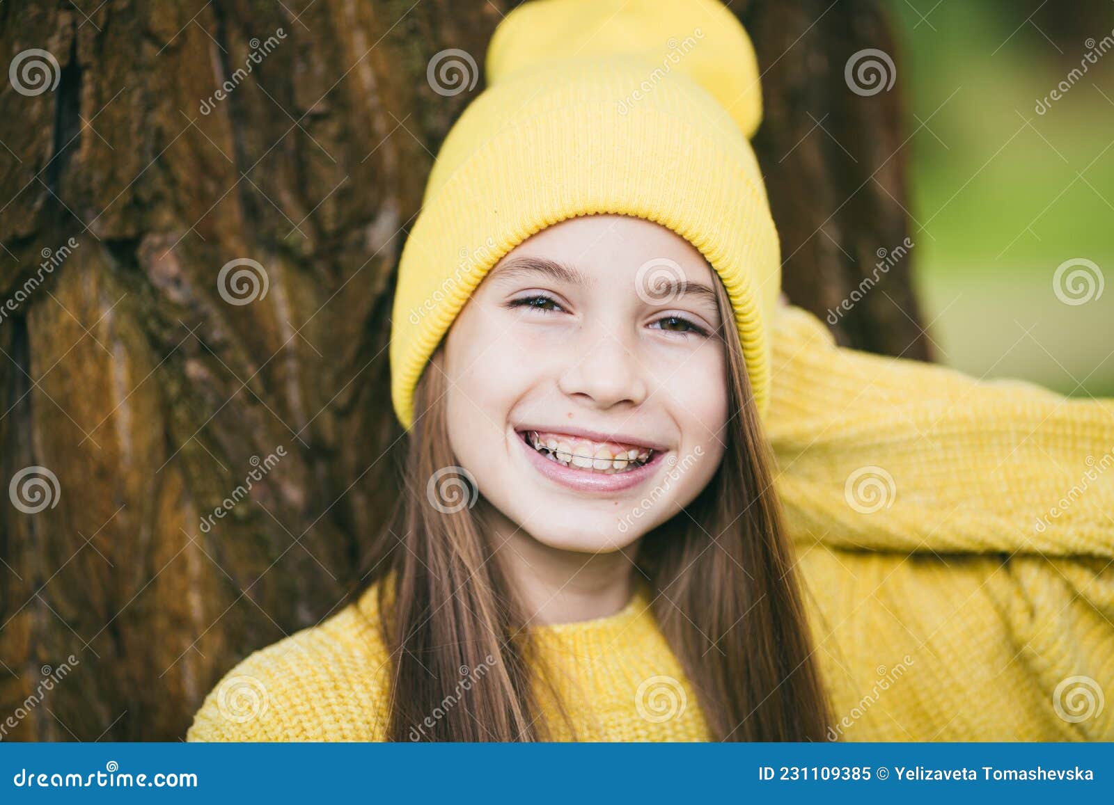 Portrait of modern happy teen girl with dental braces dressed in yellow clothes in park. Pretty teenage girl wearing braces smiling cheerfully. Kid girl in autumn smiling with braces teeth apparatus.