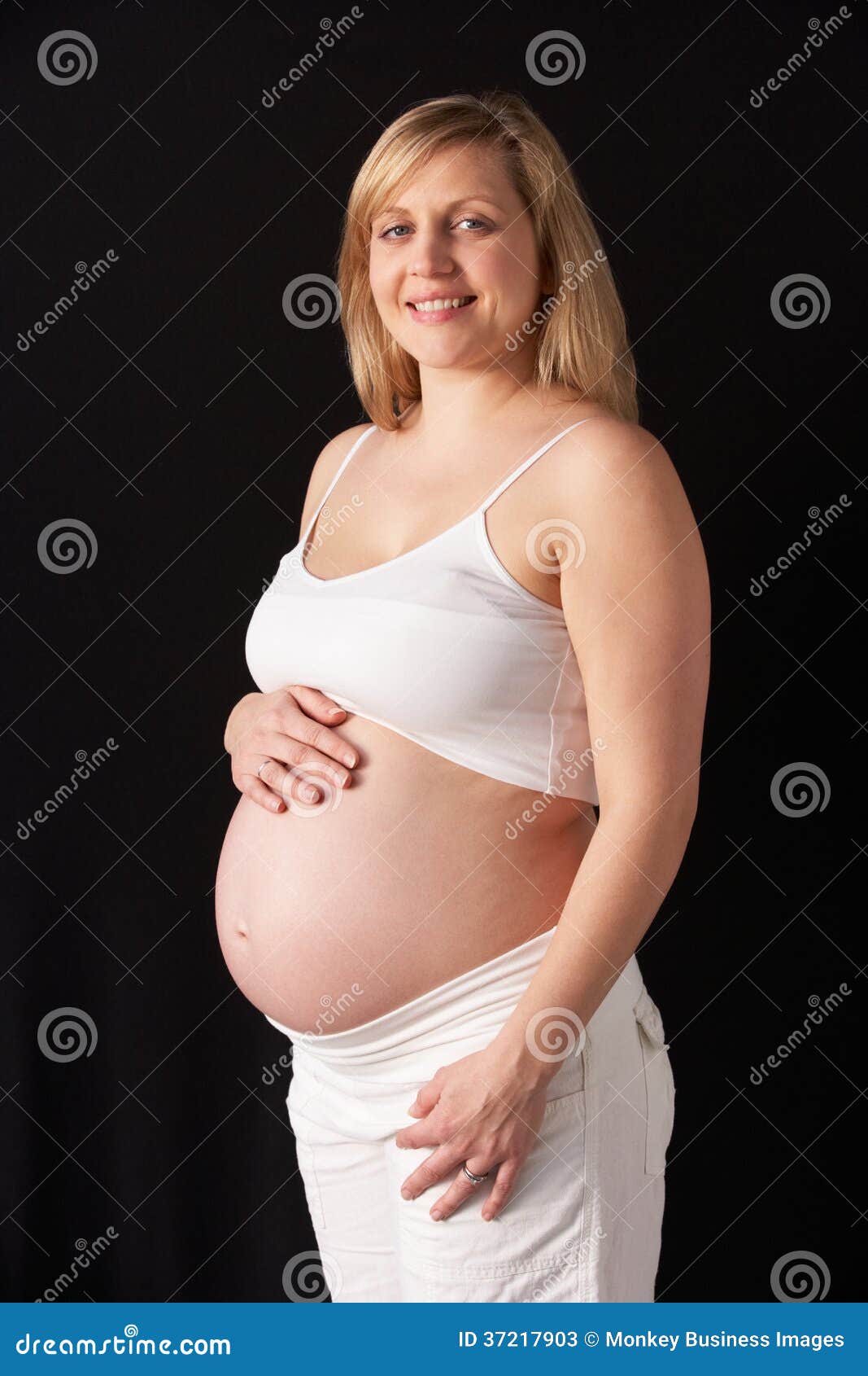 portrait of 6 months pregnant woman wearing white on black background