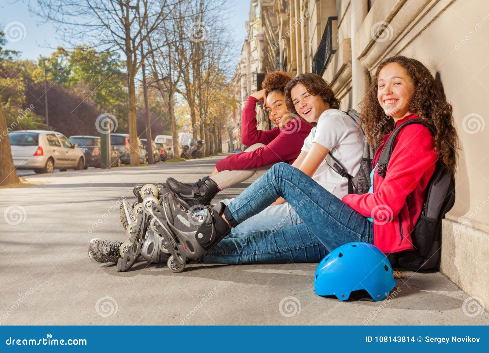 happy teens with rollerblades sitting at sidewalk