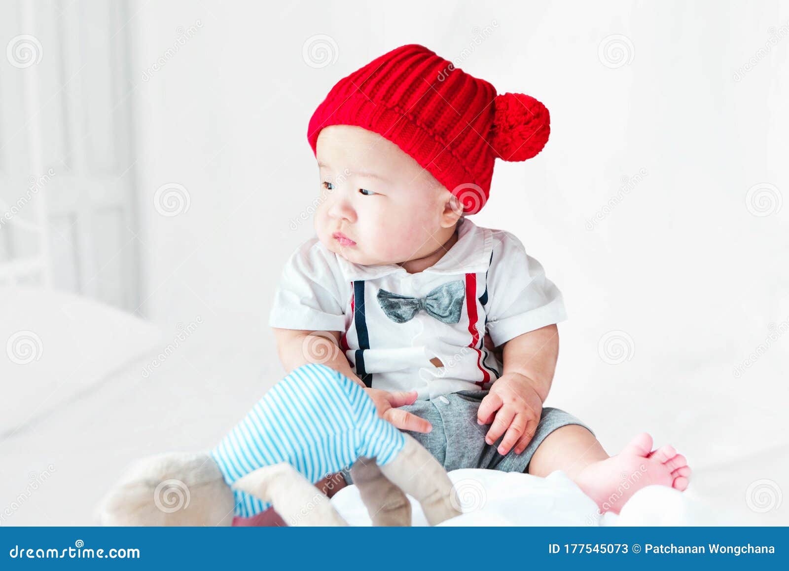 portrait of a newborn asian baby, a child wore a suit and a red wool hat sit ting on bedroom, cute and smilingly
