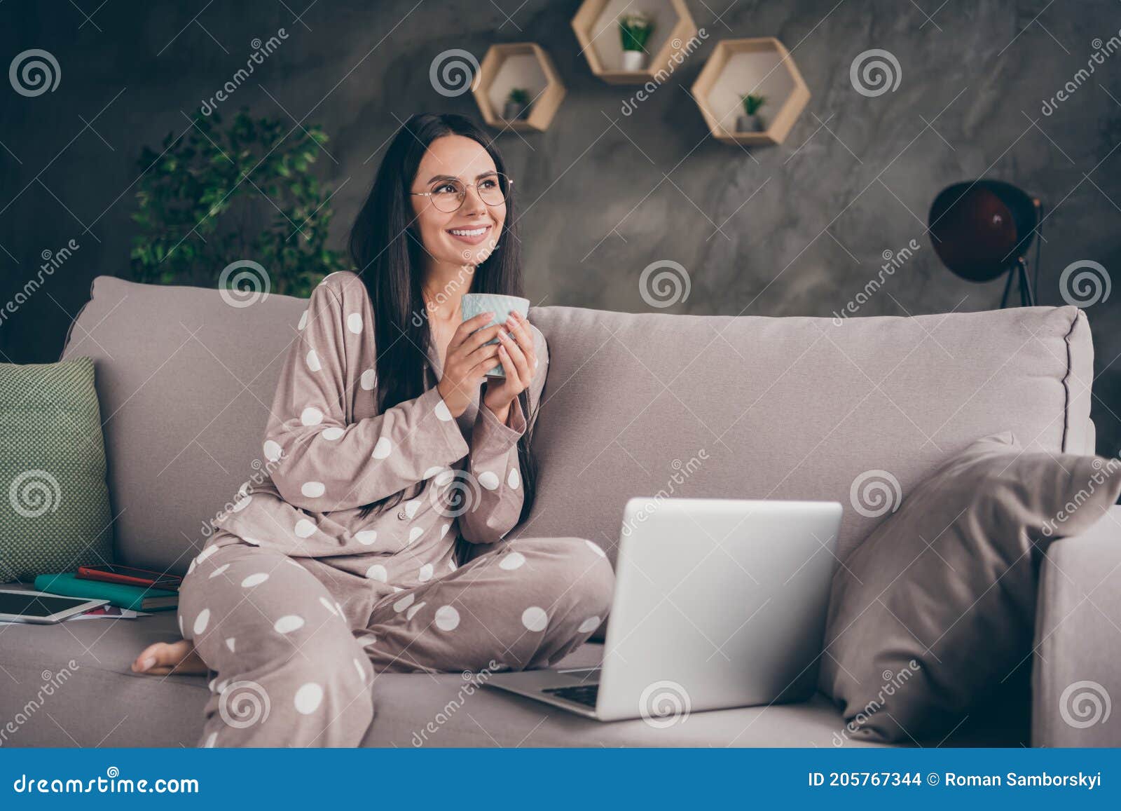 portrait of nice optimistic girl hold cup look empty space wear spectacles pijama at home on sofa