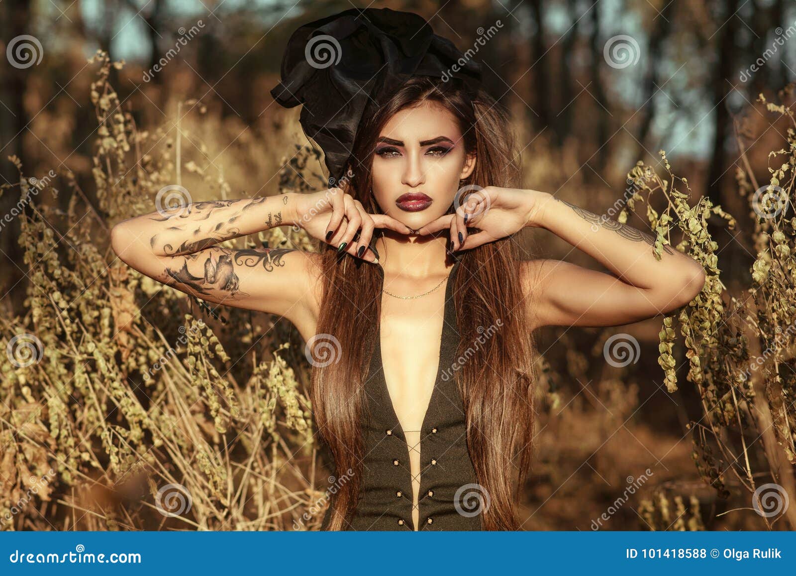 portrait of a posh dangerous tattooed witch wearing corset dress and vintage silk hat standing in the woods