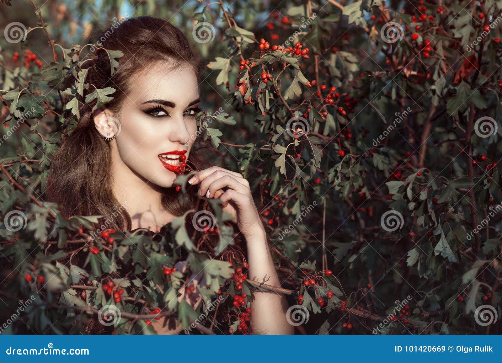 portrait of posh woman with provocative make up and predatory gaze standing in the berry bush and eating red berries