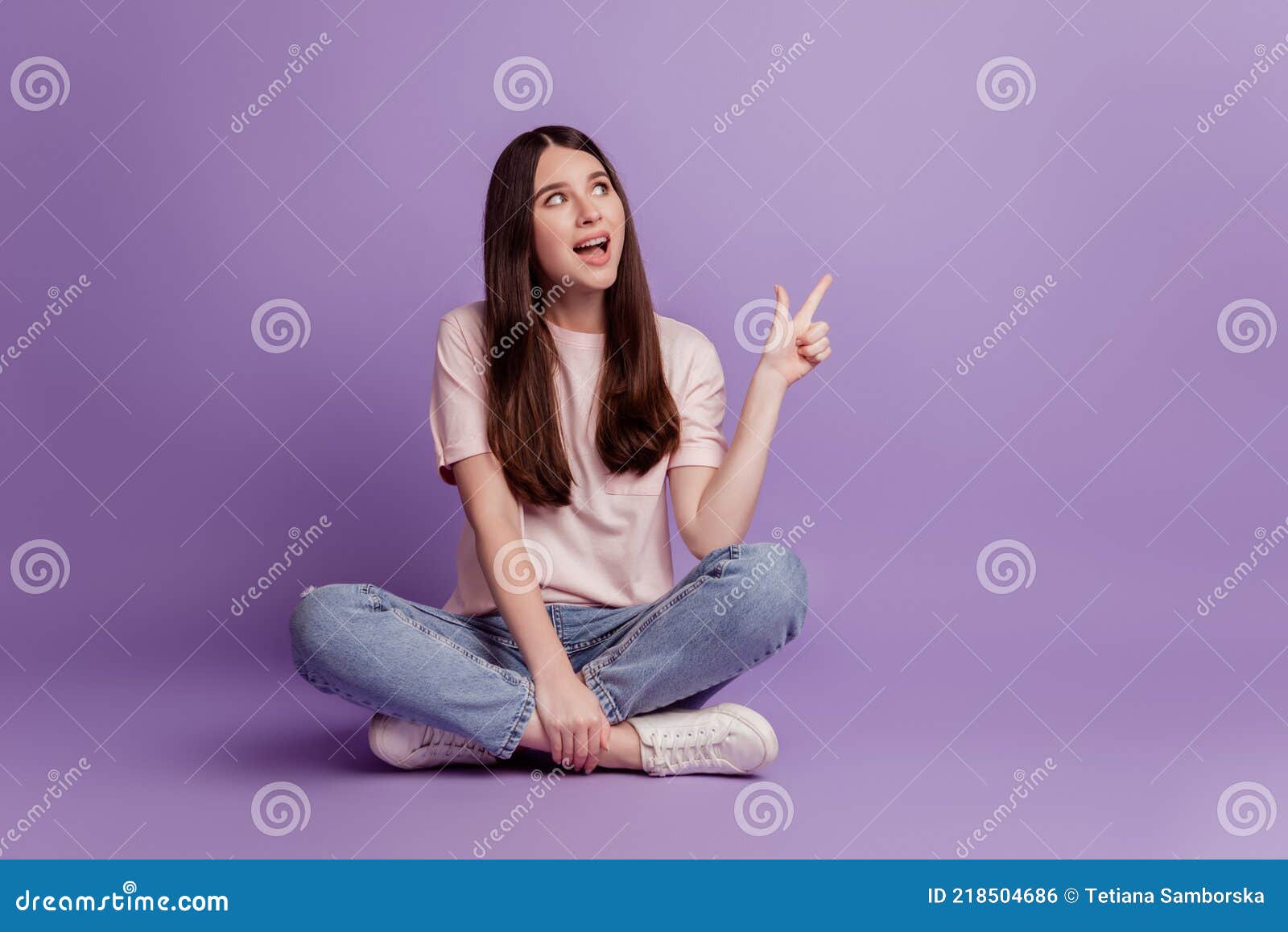 Portrait of a Pretty Girl Pointing Finger Away Sit Floor on Purple Wall ...