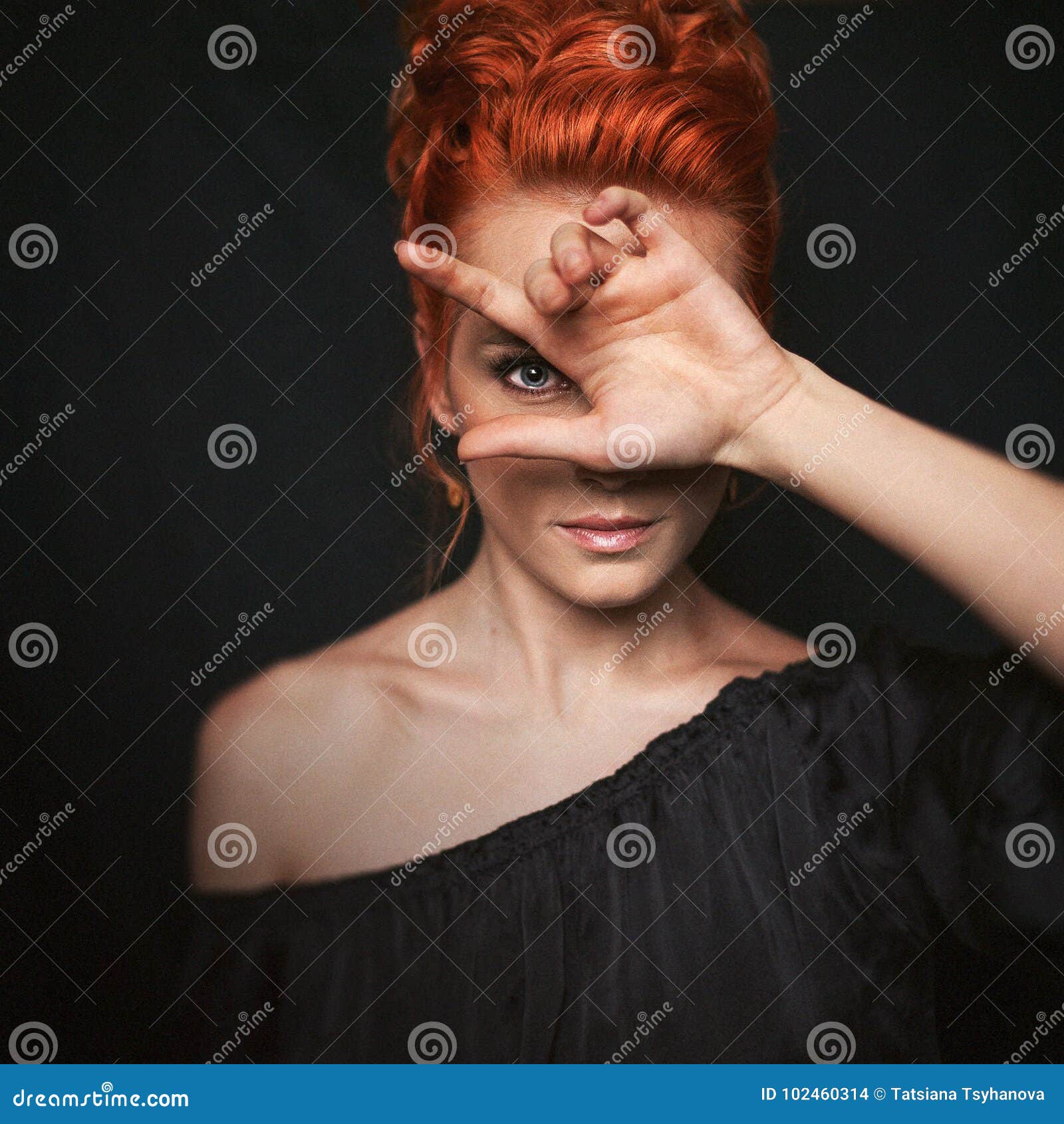 portrait of redhead woman with blue eyes. girl looks directly into the camera through her fingers.