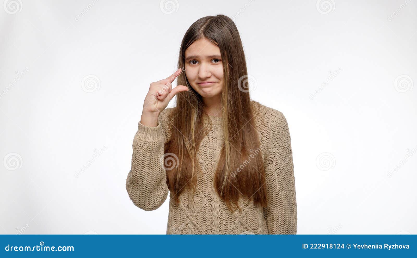 portrait of sceptic girl showing small size with hand over white studio background