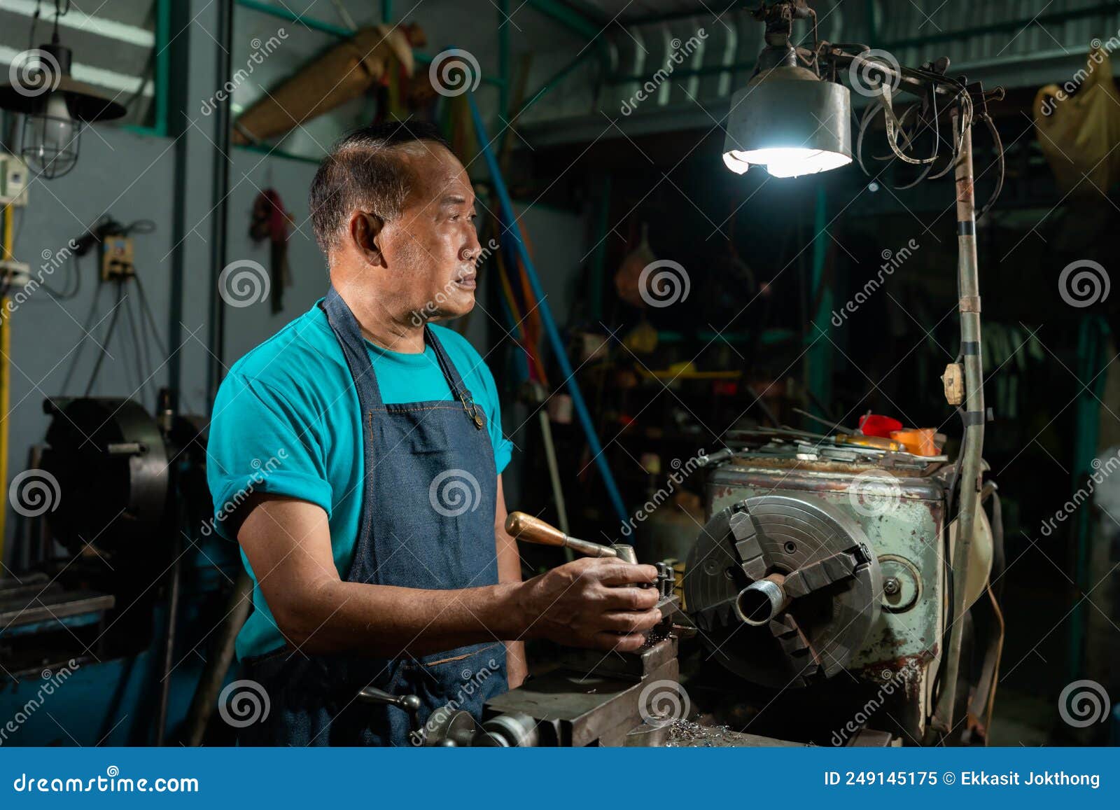 portrait of a senior asian man who is a steelworker. using a small steel turning tool to prepare for a lathe job in my family`s